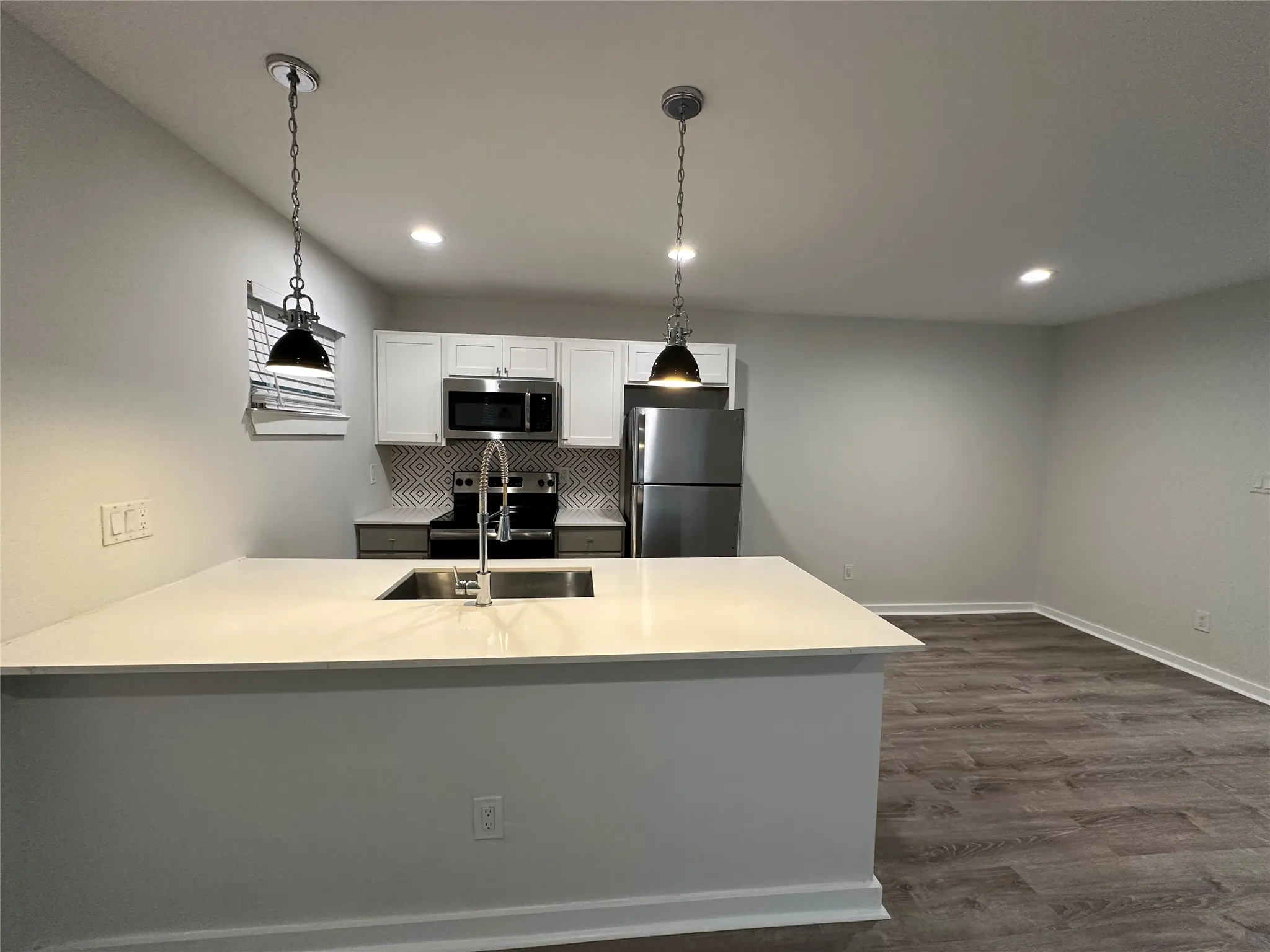 Kitchen featuring a central island with an undermount sink, pendant lighting, white upper cabinetry, stainless steel appliances, and wood-finish flooring