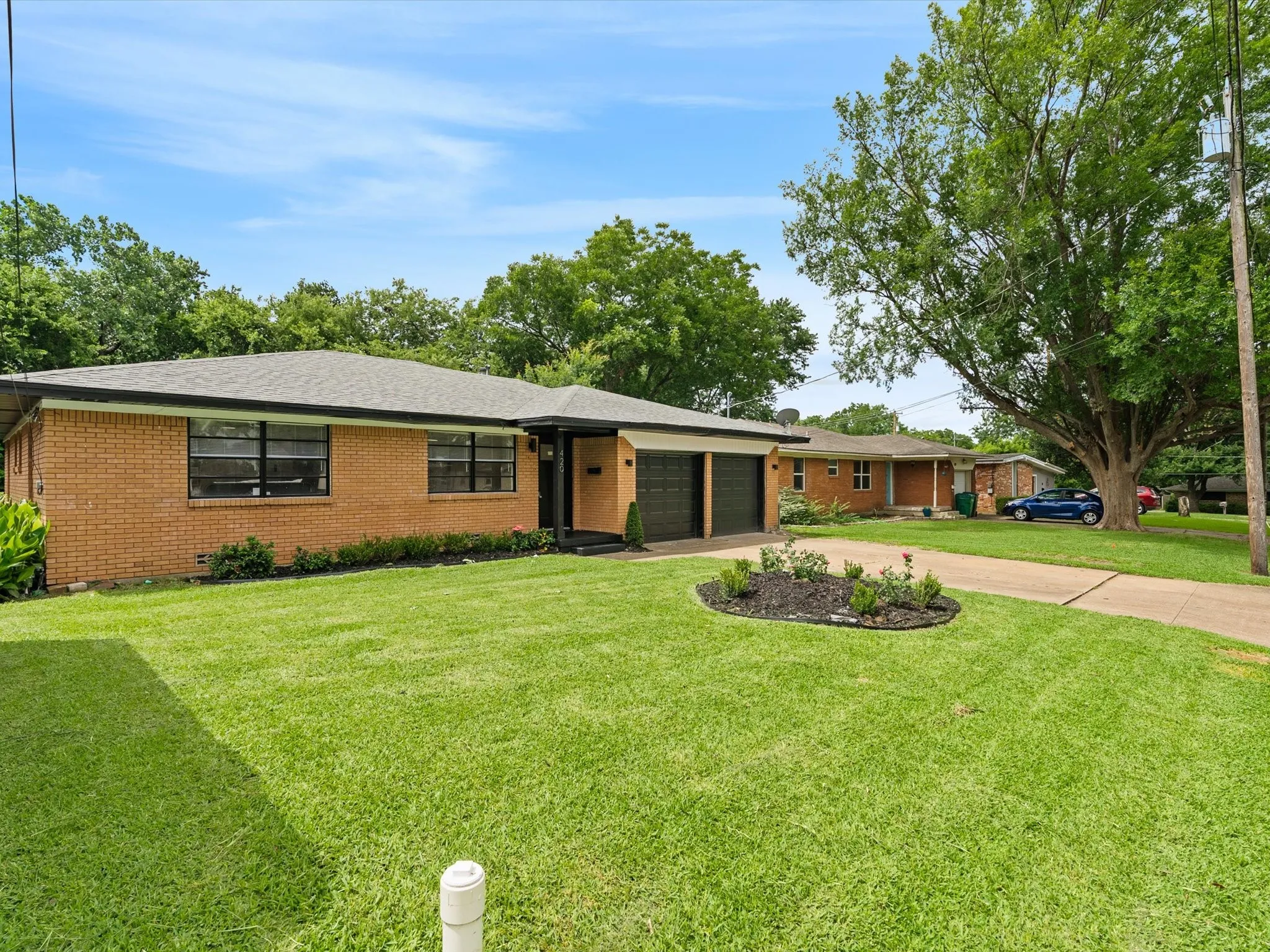 Super cute renovation with a large front yard, large driveway, refreshed landscaping, and painted garage doors and trim.
