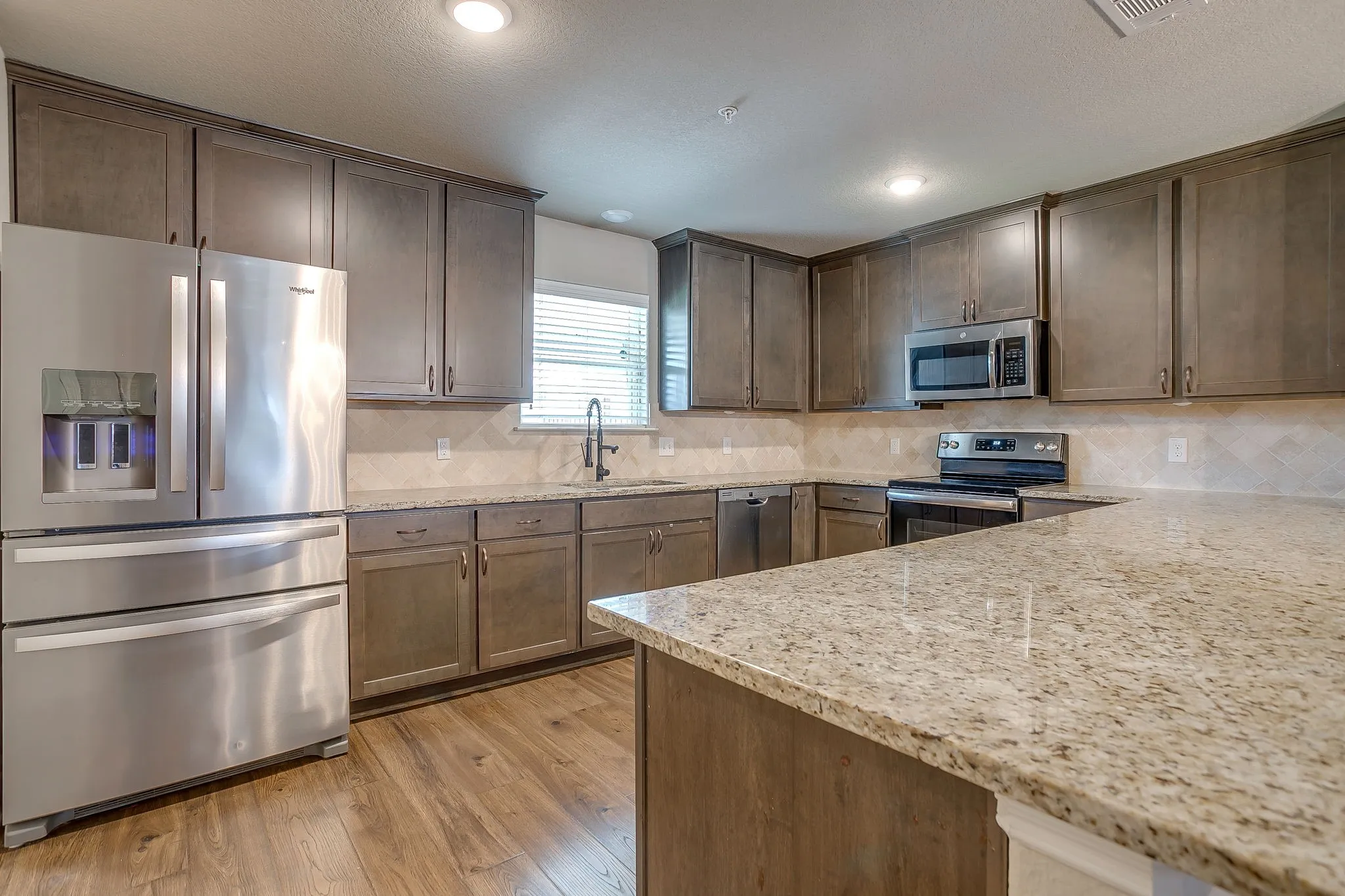Kitchen featuring wood-finish flooring, abundant cabinetry, stainless steel appliances, granite countertops, and a tiled backsplash