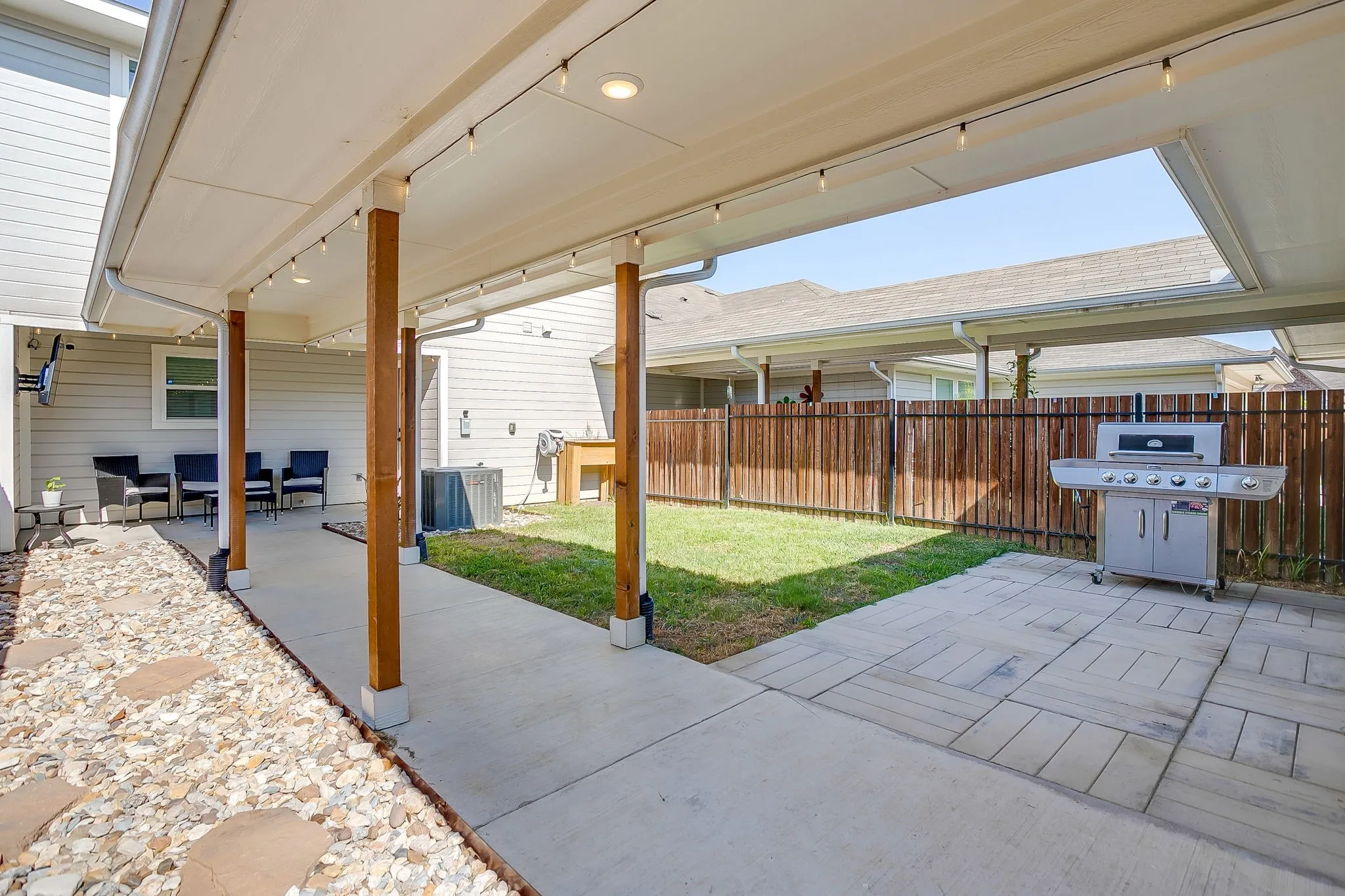 Covered patio area featuring concrete flooring, string lighting, and a fenced yard with a manicured lawn