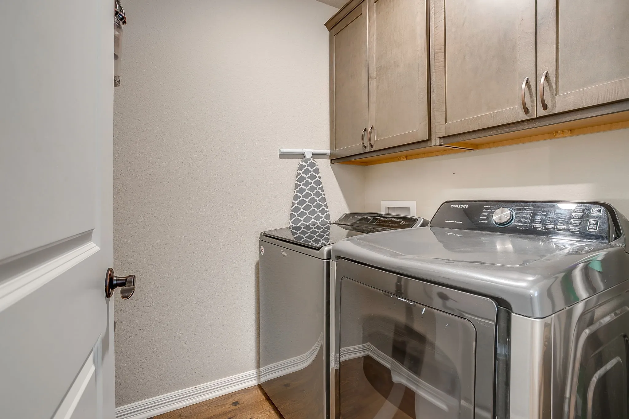 Dedicated laundry area featuring overhead cabinetry, wood-finish flooring, and light-toned walls
