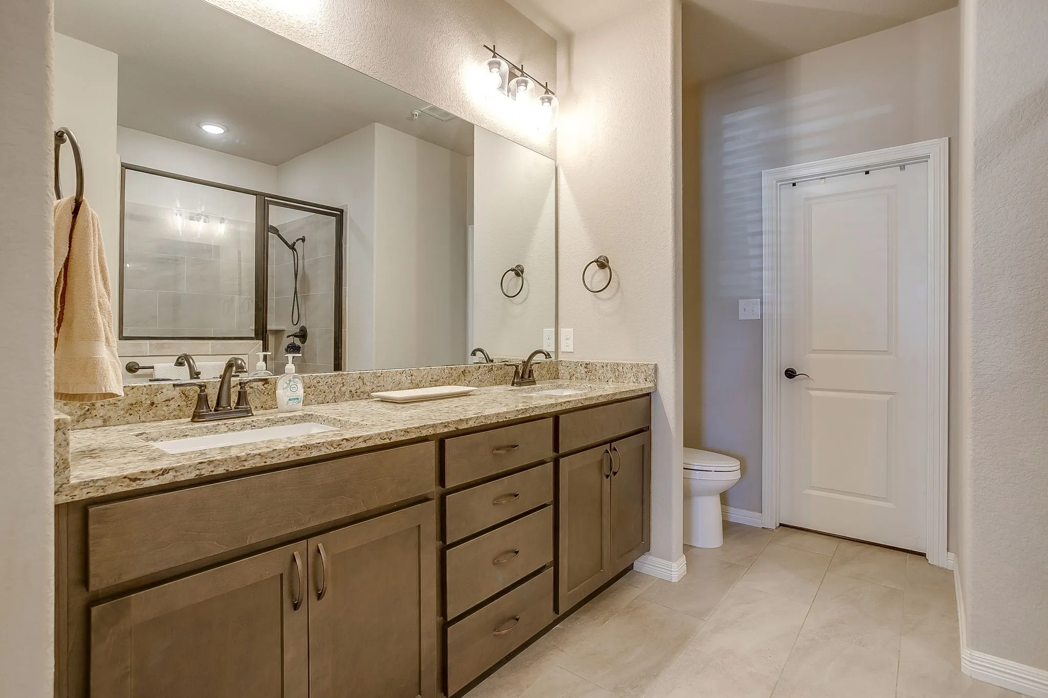 Bathroom featuring a dual vanity with granite countertops, undermount sinks, and bronze-finish fixtures