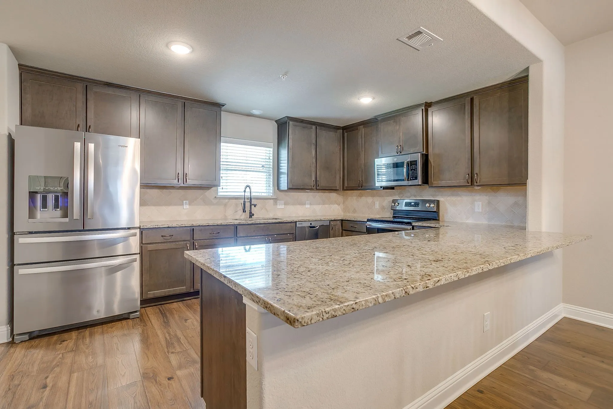 Kitchen featuring extensive cabinetry, stainless steel appliances, granite countertops, and wood-finish flooring