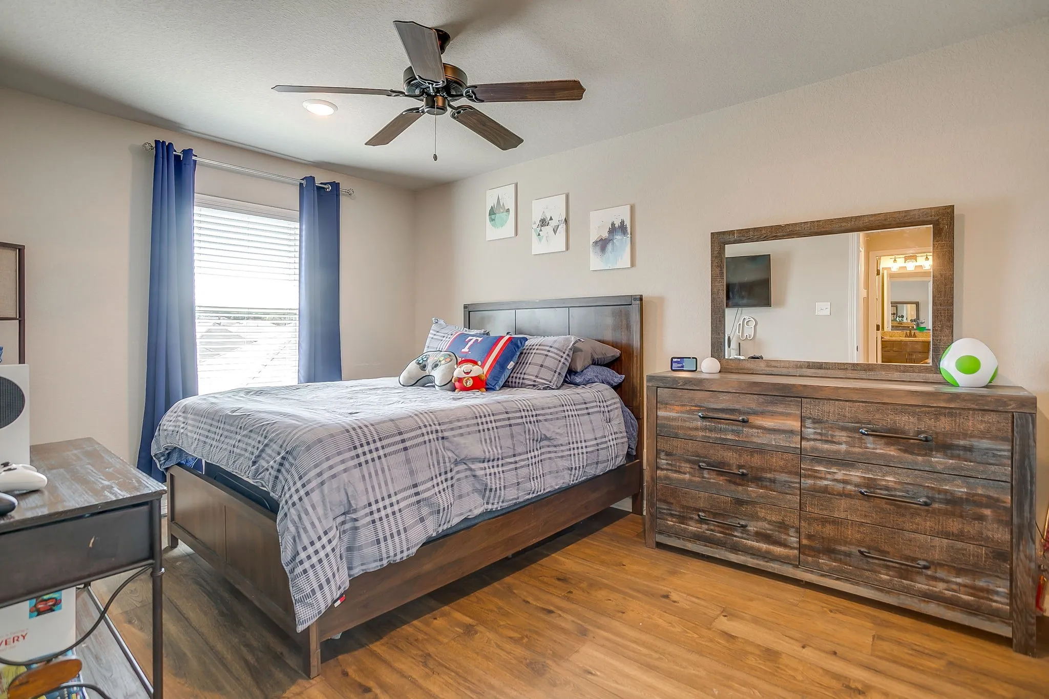 Wood-finish flooring throughout, featuring a window with blinds, a ceiling fan with integrated lighting, and neutral wall tones