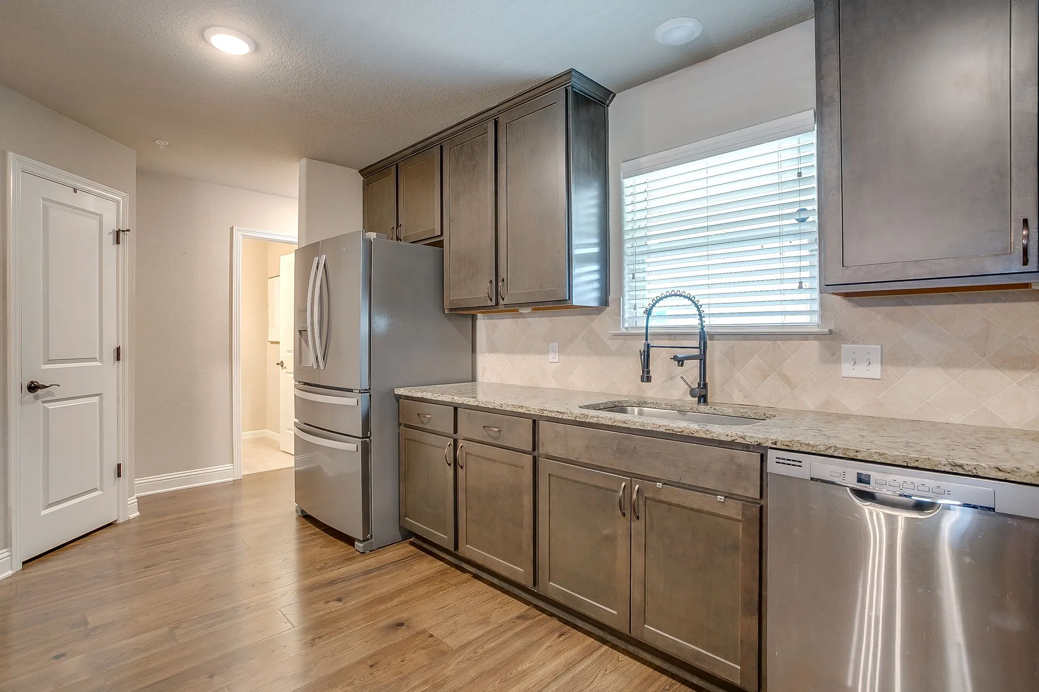 Contemporary kitchen featuring wood-finish flooring, ample cabinetry, stainless steel appliances, a stone-look countertop, and a tiled backsplash