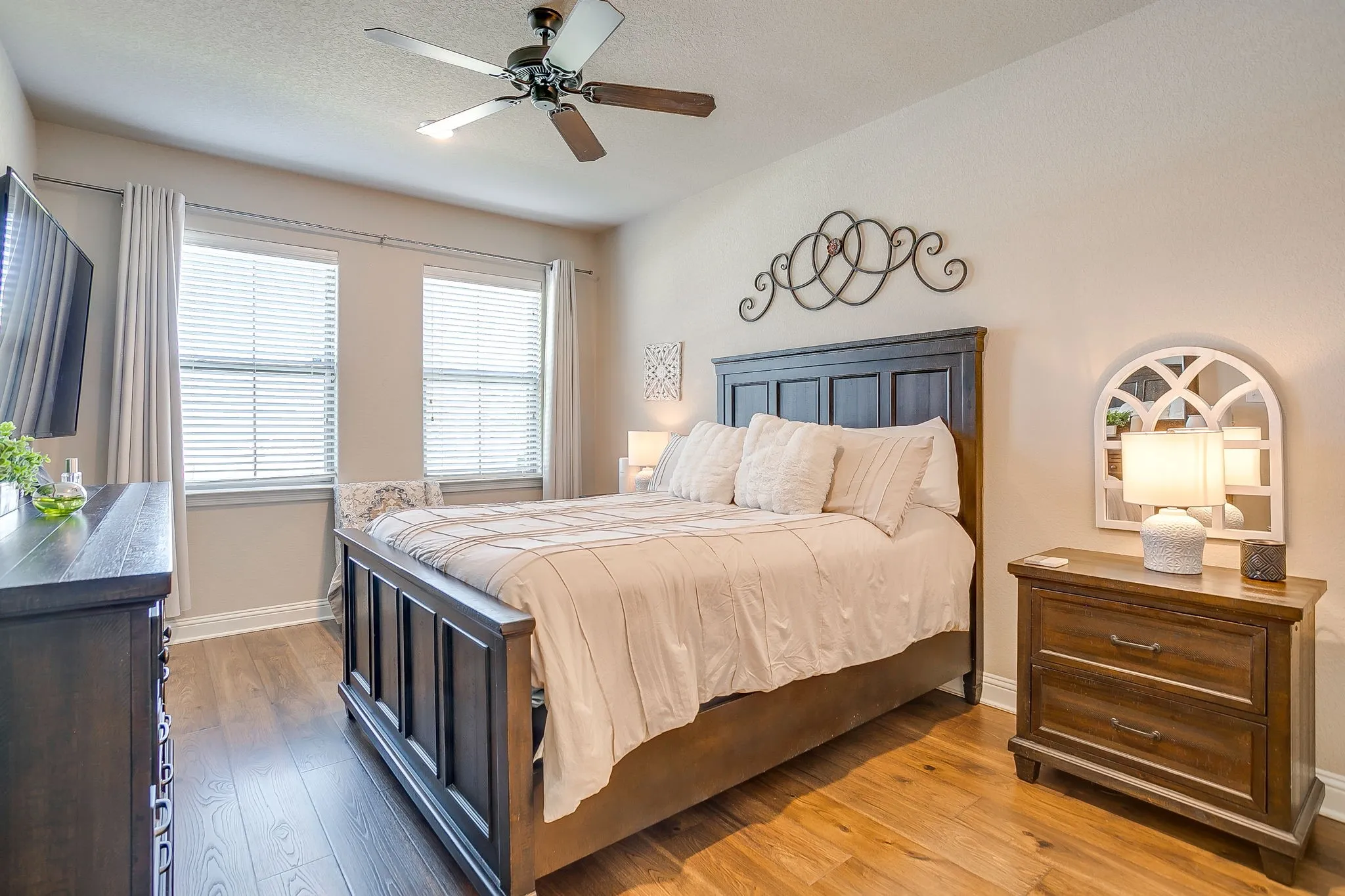 Bright interior space featuring wood-finish flooring, two windows with blinds and drapes, a ceiling fan with integrated lighting, and neutral wall tones