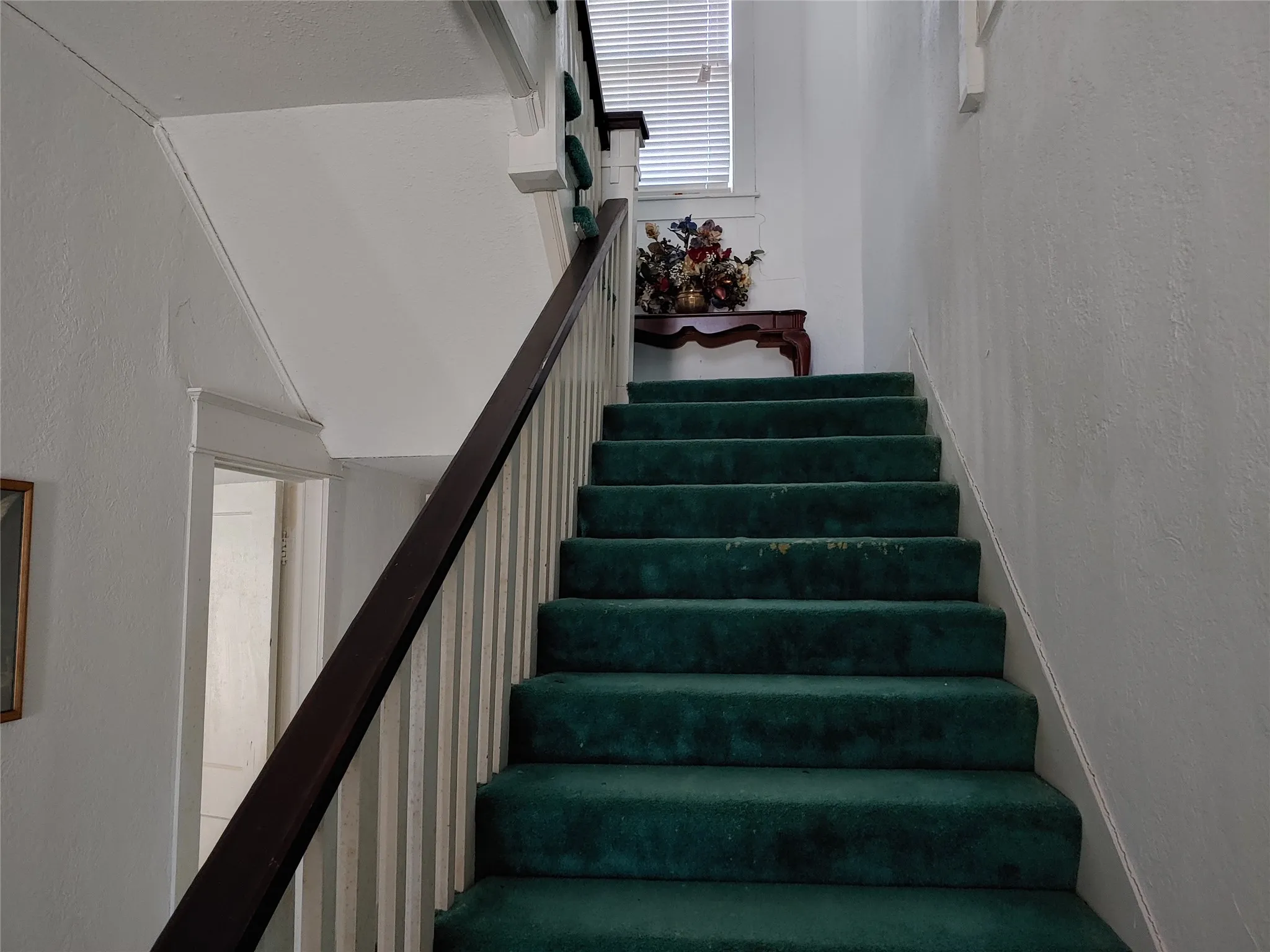 Staircase featuring green carpet treads, white painted risers, a dark wood-finish handrail, and white balusters
