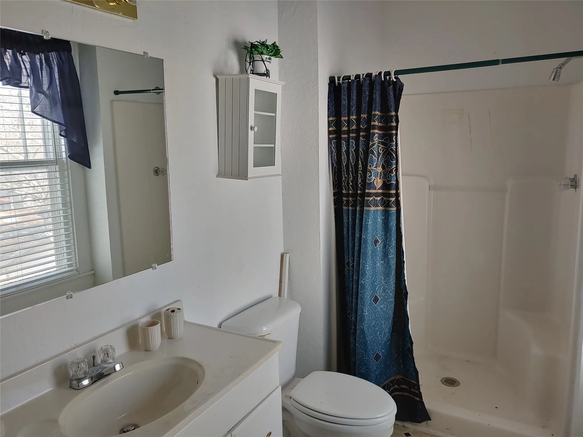 Bathroom featuring a single vanity, wall-mounted mirror, white wall cabinet, and a walk-in shower with an integrated bench seat