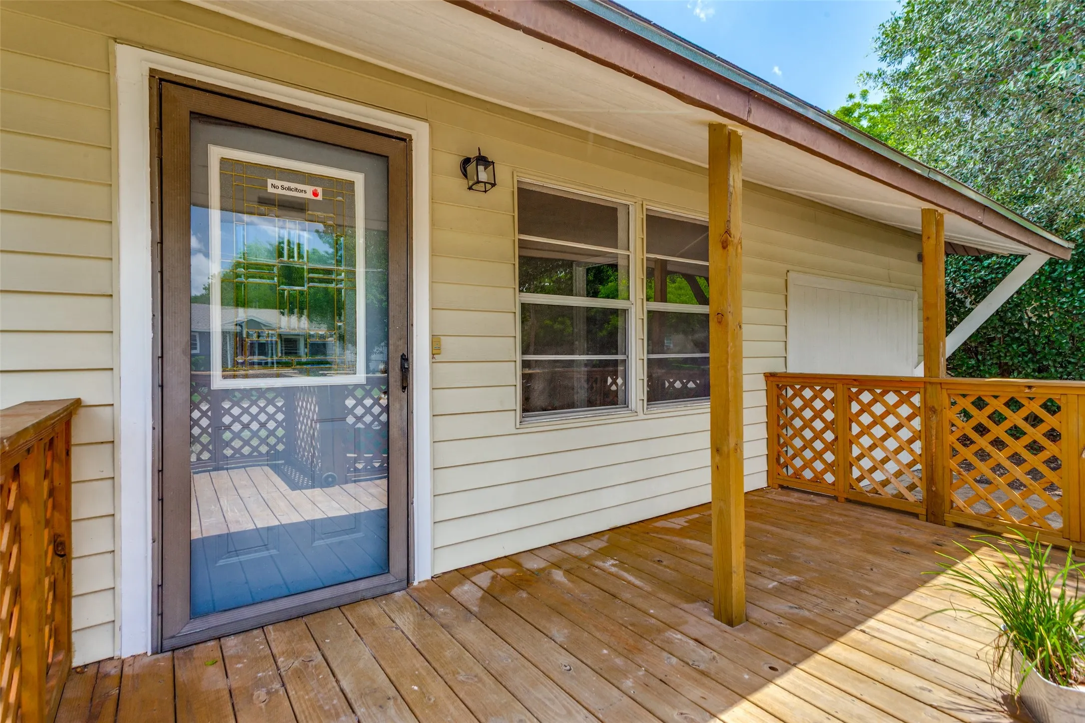 Expansive exterior deck featuring natural wood-finish flooring, a full-view storm door, and decorative lattice railing