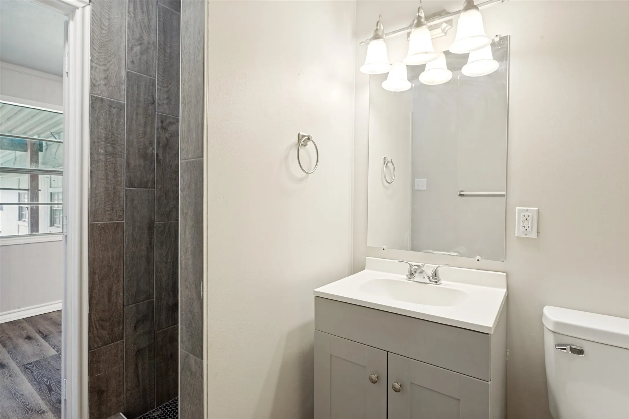 Bathroom featuring a single vanity with an integrated sink, a rectangular mirror, and a four-light fixture