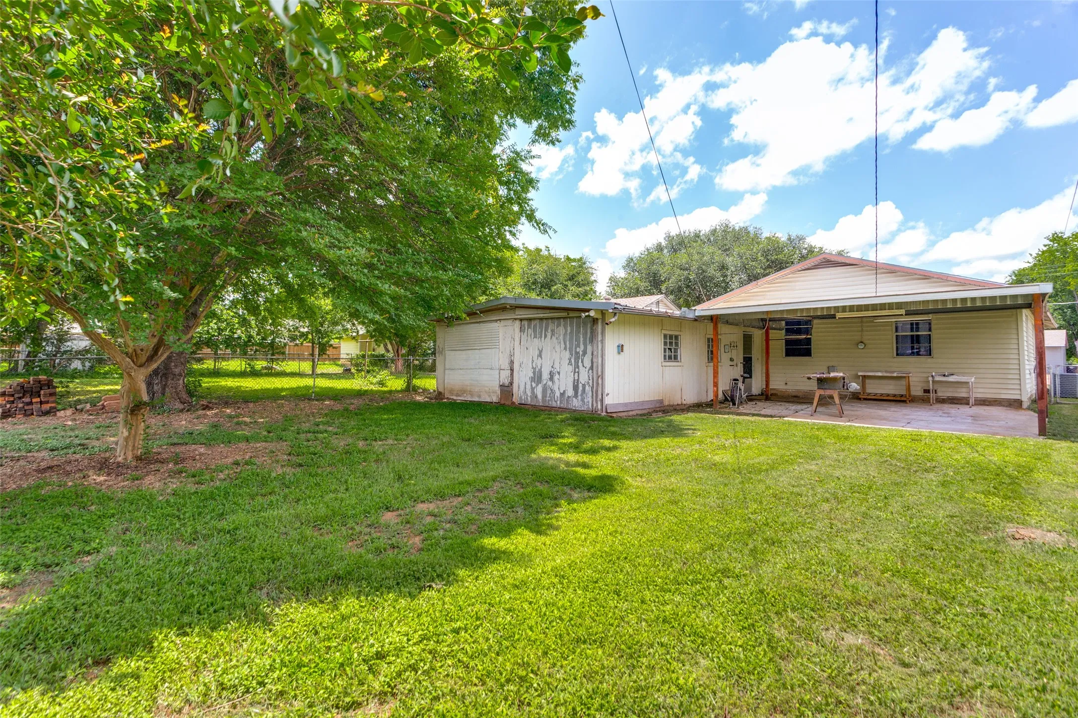 Expansive rear yard featuring a large tree, a detached storage building, and a covered patio with a concrete surface