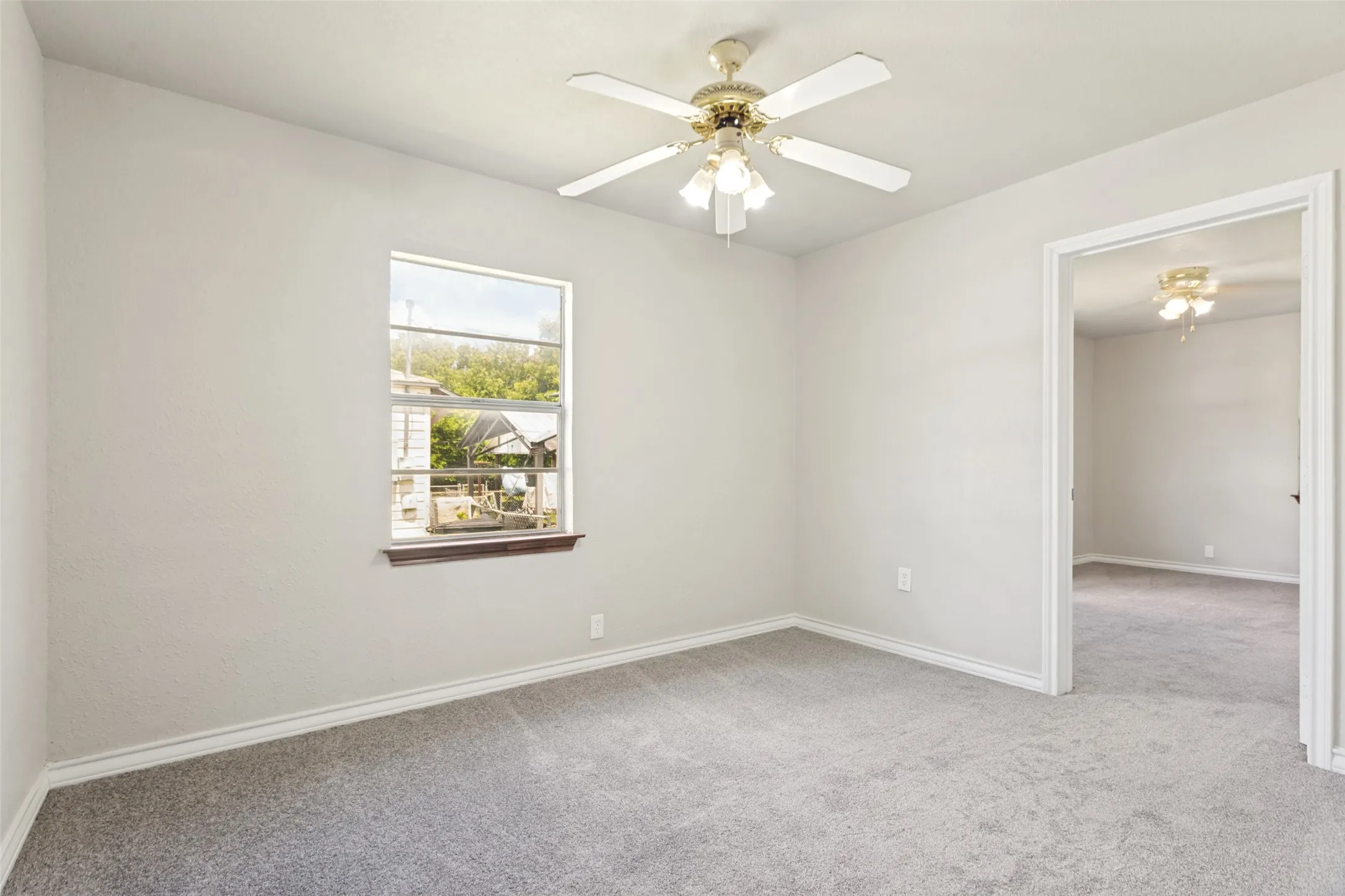 Carpeted interior room with light gray walls, white trim, a single window, and a ceiling fan with integrated lighting