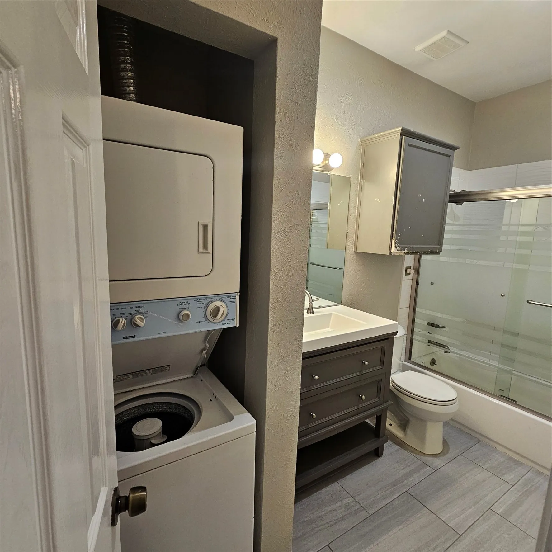 Full bathroom featuring estacked washer and dryer, shower / bath combination with glass door, vanity, and a textured wall