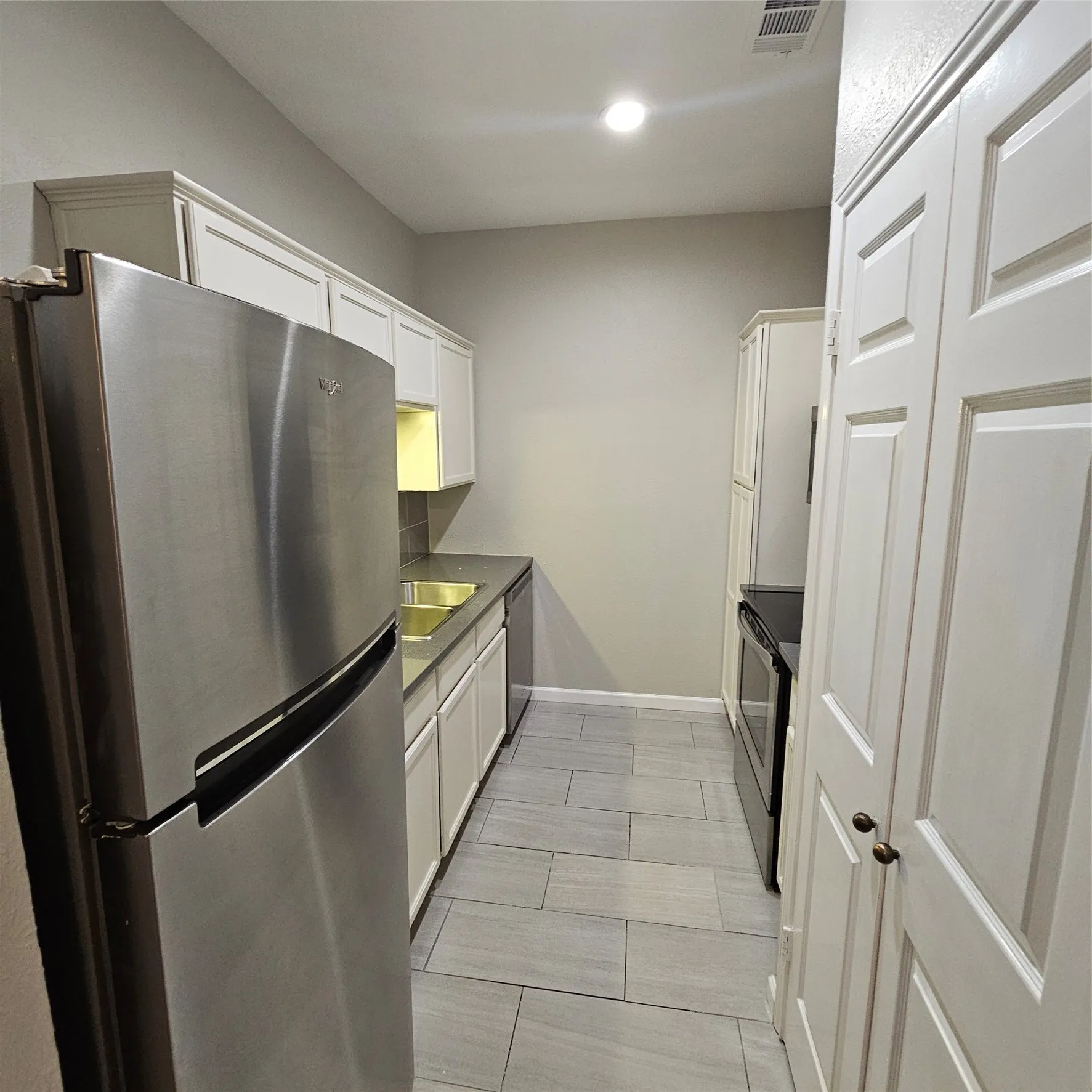 Kitchen with fridge, stove, white cabinetry, dishwashing machine, and recessed lighting