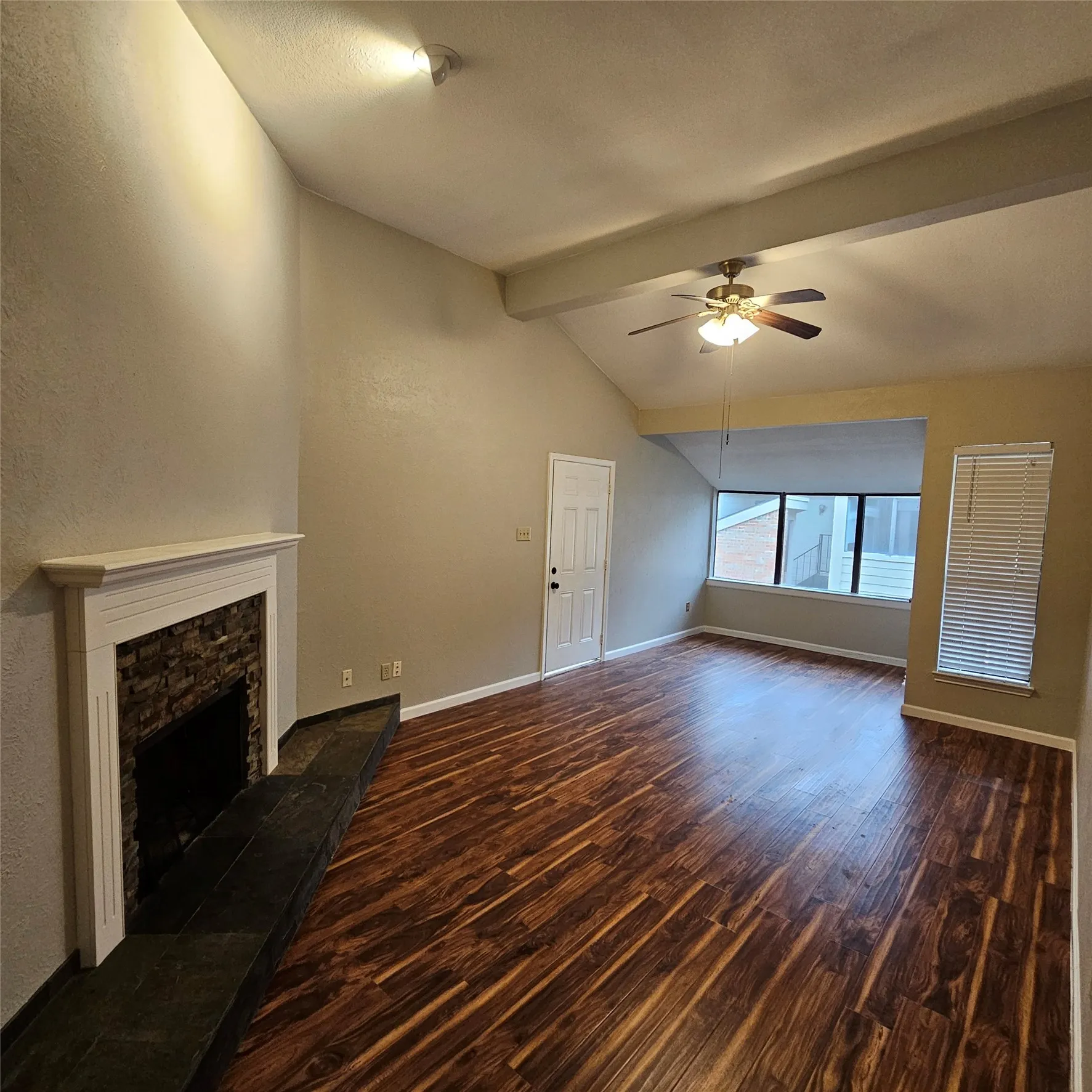 Unfurnished living room with wood finished floors, ceiling fan, a fireplace, and a textured wall