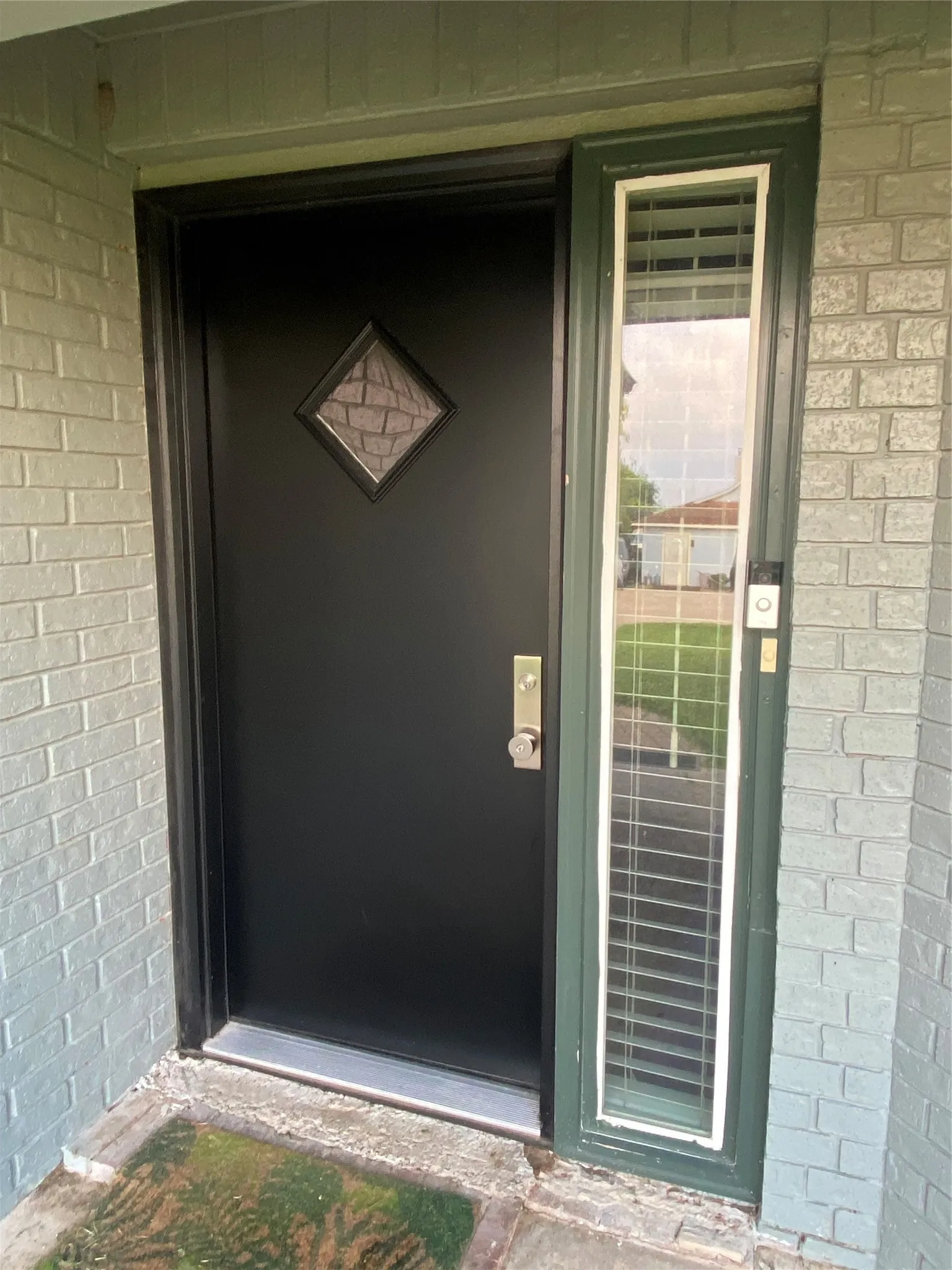 Black custom entry door with a decorative diamond-shaped window, brushed nickel hardware, and an adjacent sidelight with horizontal blinds