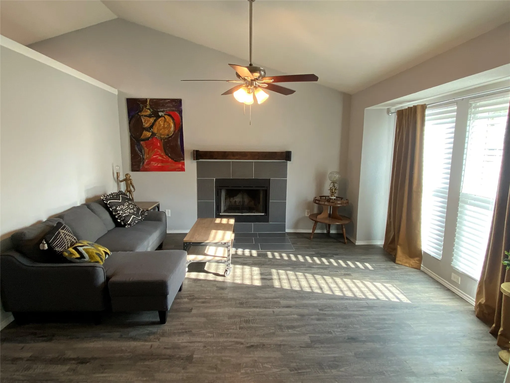 Living area featuring vaulted ceilings, a contemporary fireplace with a dark tile surround and multiple windows with custom blinds