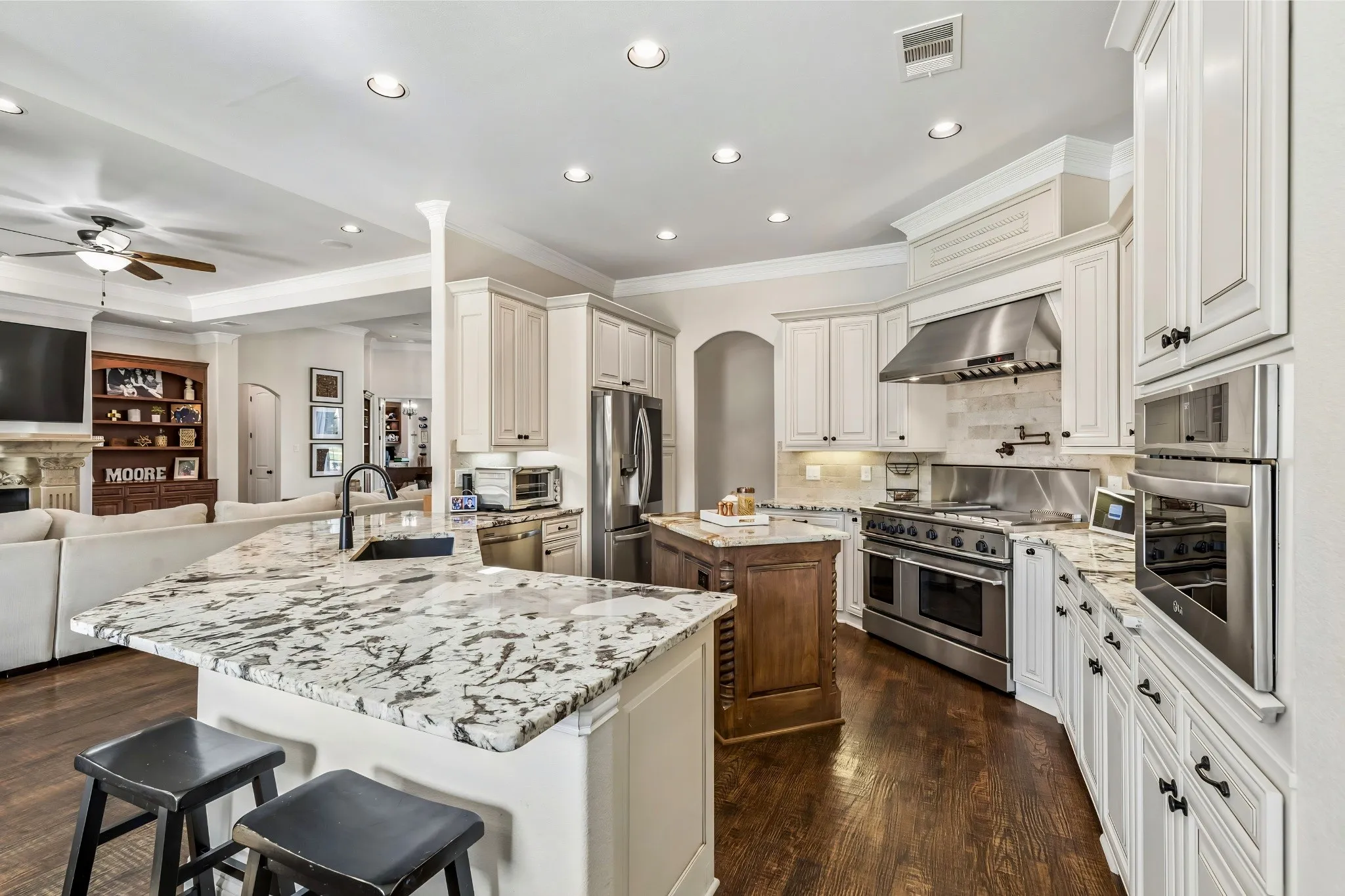Spacious kitchen featuring white cabinetry, stone countertops, stainless steel appliances, a center island, and wood-finish flooring