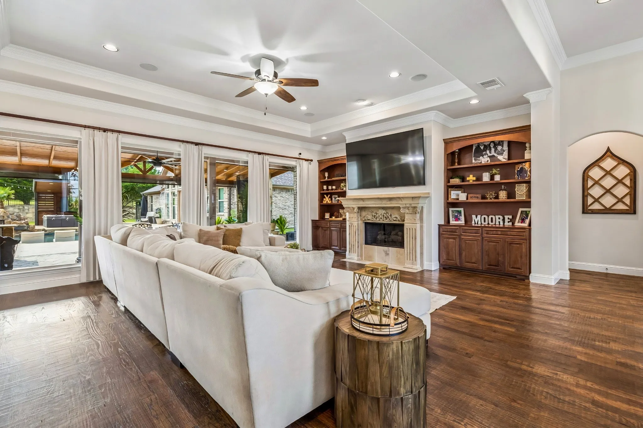 Wood-finish flooring, recessed lighting, crown molding, built-in shelving, and a stone fireplace