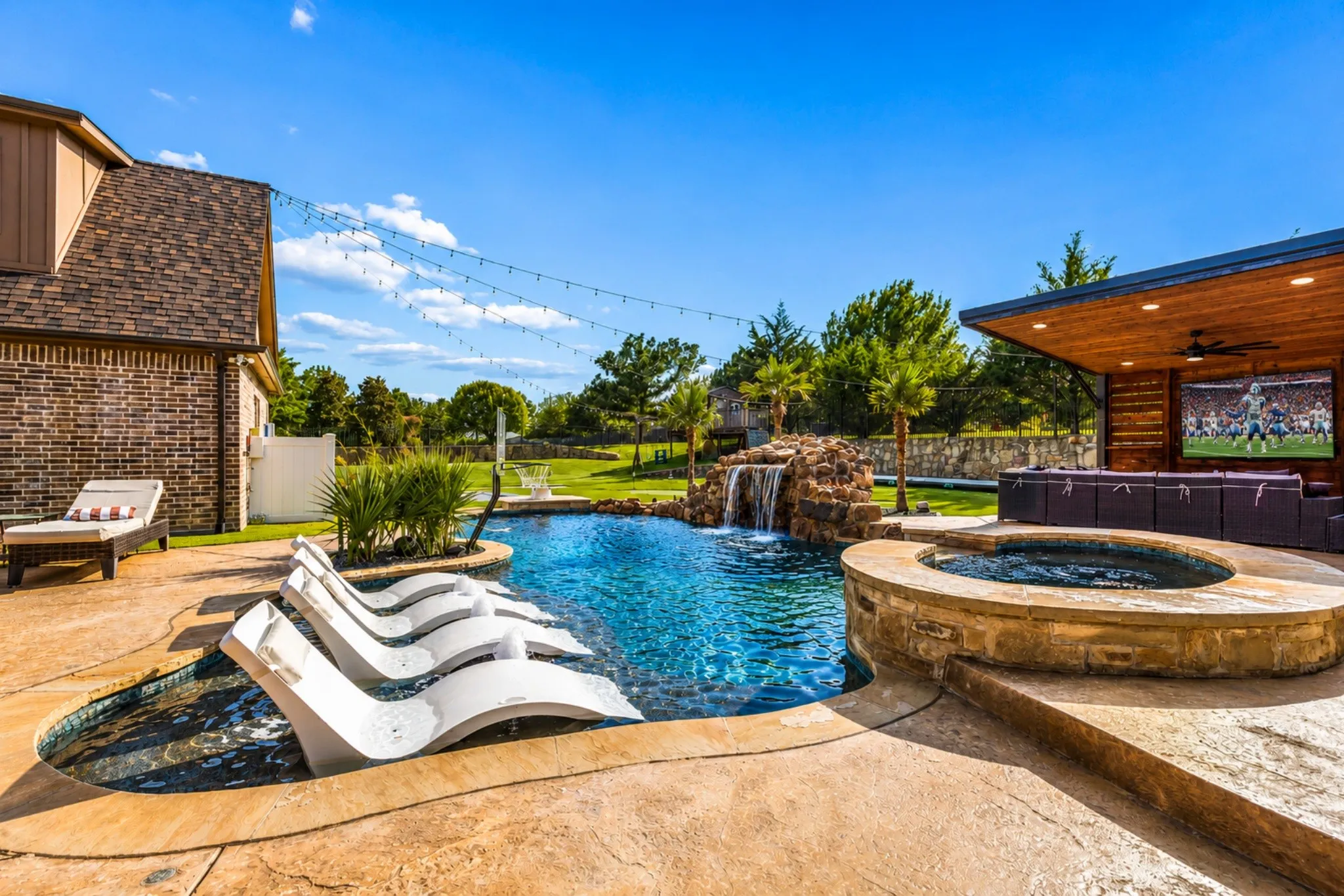Resort-style backyard oasis featuring a resort-style swimming pool with cascading waterfall, lounging area with built-in seating, circular fire pit with stone surround, covered entertainment pavilion with wood ceiling, mature landscaping, and manicured lawn