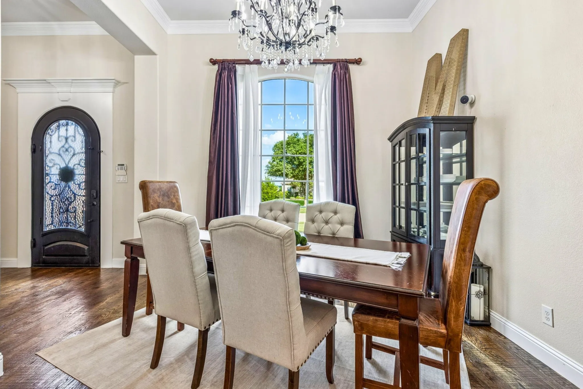 Ornate wrought iron arched entry door, wood-finish flooring, arched window, crystal chandelier, and a built-in display cabinet