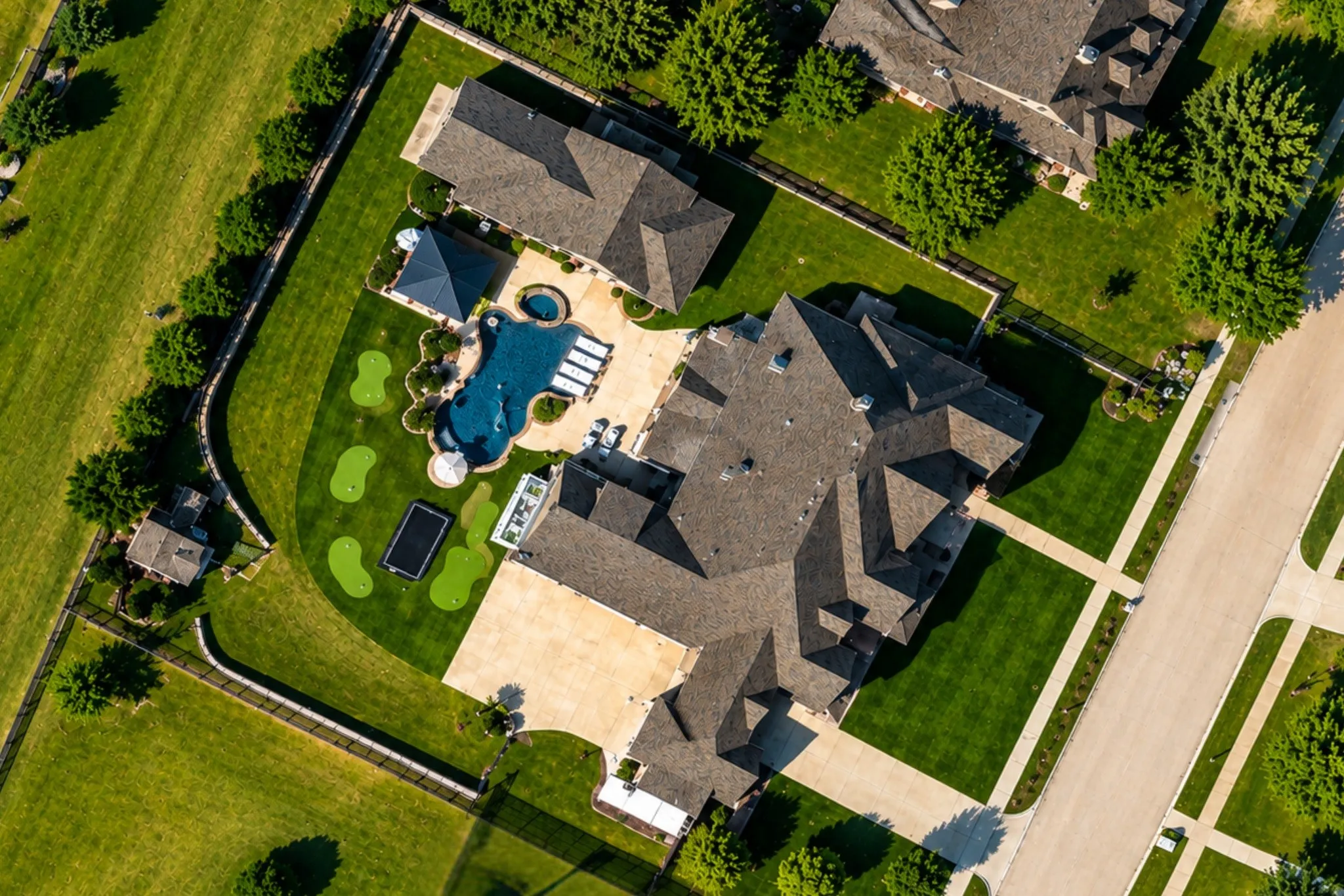 Expansive property featuring a multi-gabled roofline, a large swimming pool with integrated spa, multiple putting greens, and a paved driveway