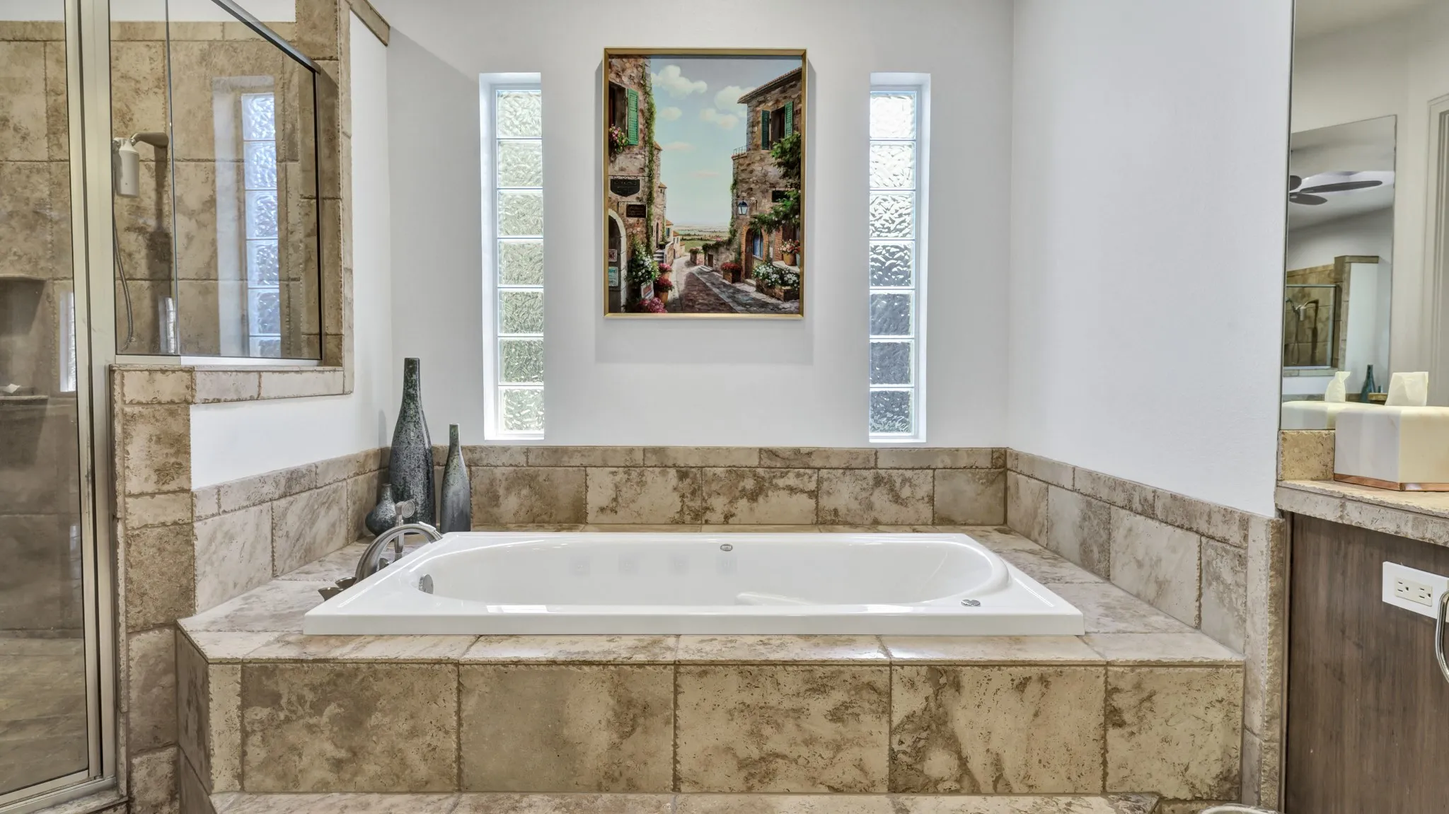 Built-in soaking tub with stone tile surround, complemented by a glass-enclosed shower