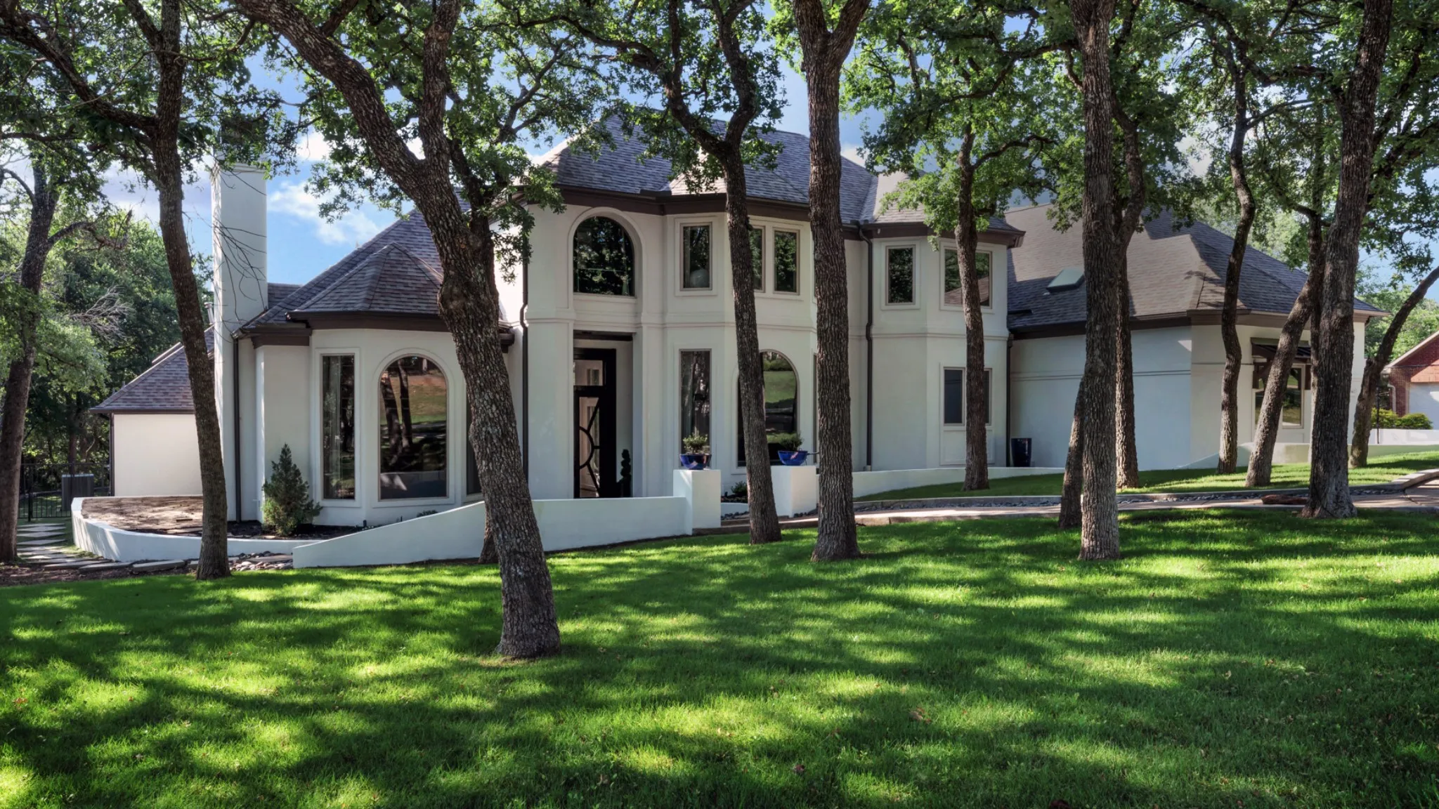 Stately white stucco exterior featuring a prominent two-story arched window, dark roofline, and an inviting front entry with a decorative dark door