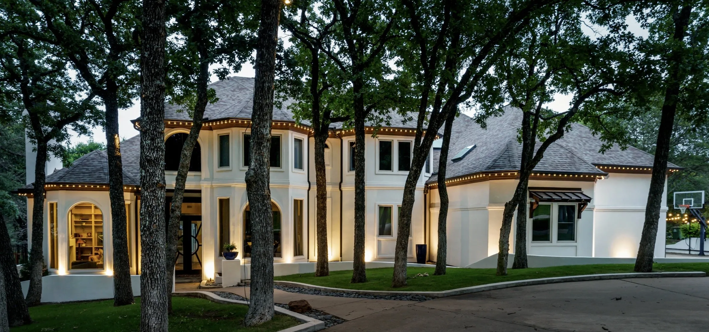 Stately architecture featuring a stucco exterior, dark shingle roofing, and extensive exterior lighting