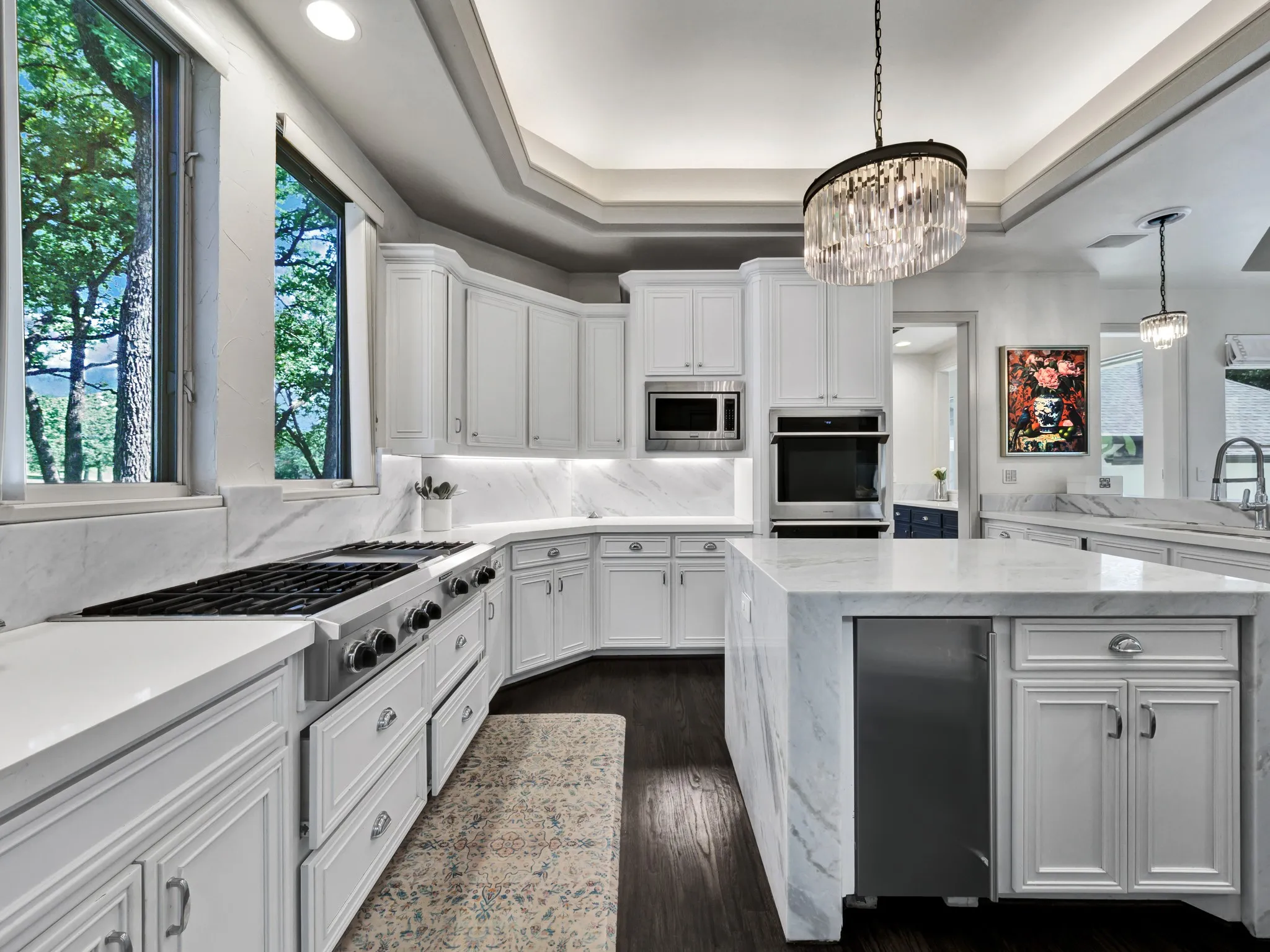 White cabinetry with under-cabinet lighting, stainless steel appliances, and wood-finish flooring