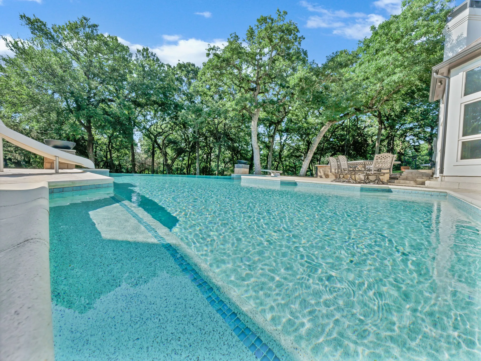 Swimming pool featuring an integrated slide, mosaic tile accents, and a surrounding hardscape