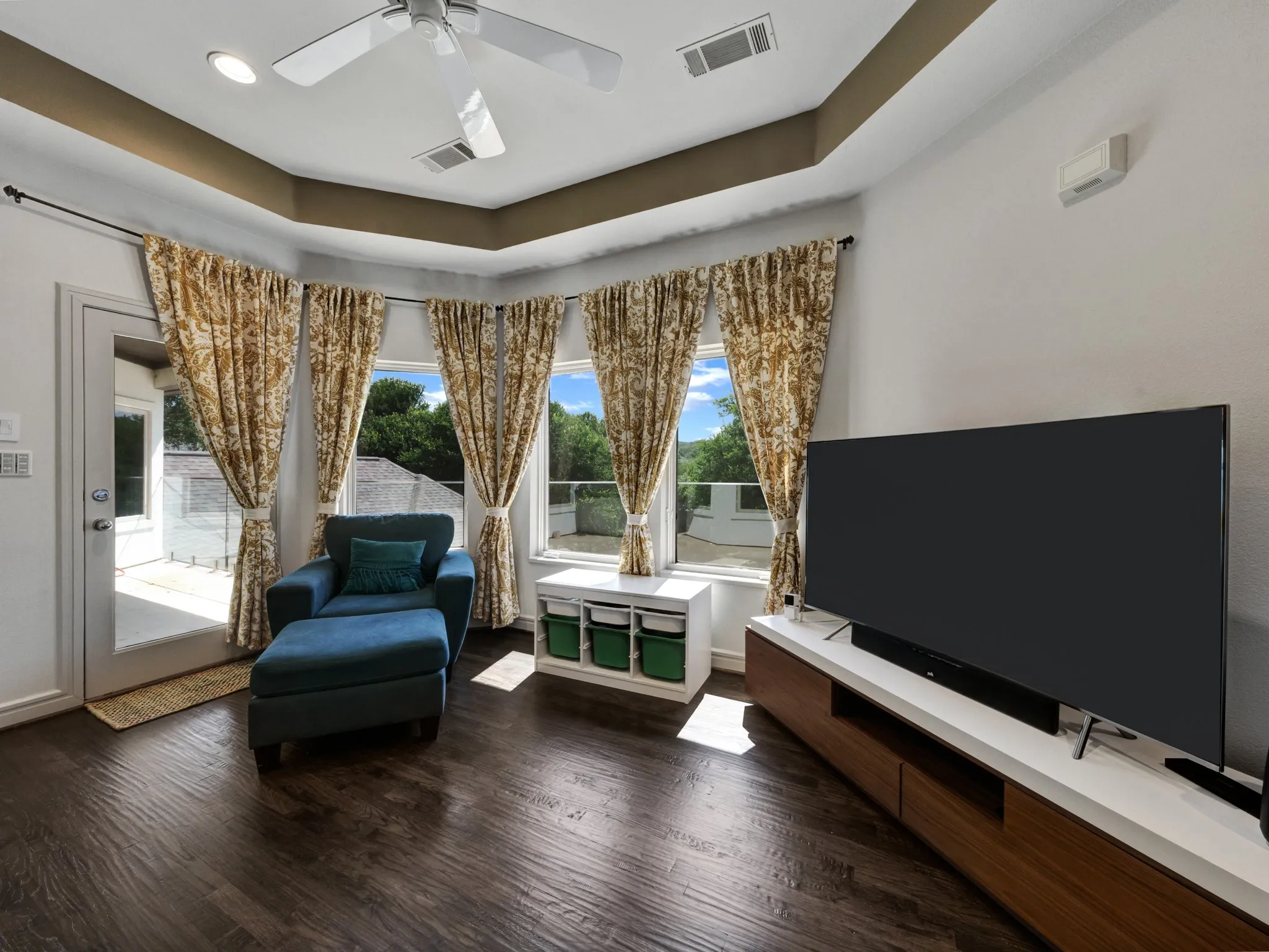 Living space featuring rich wood-finish flooring, a tray ceiling, and a ceiling fan with integrated lighting