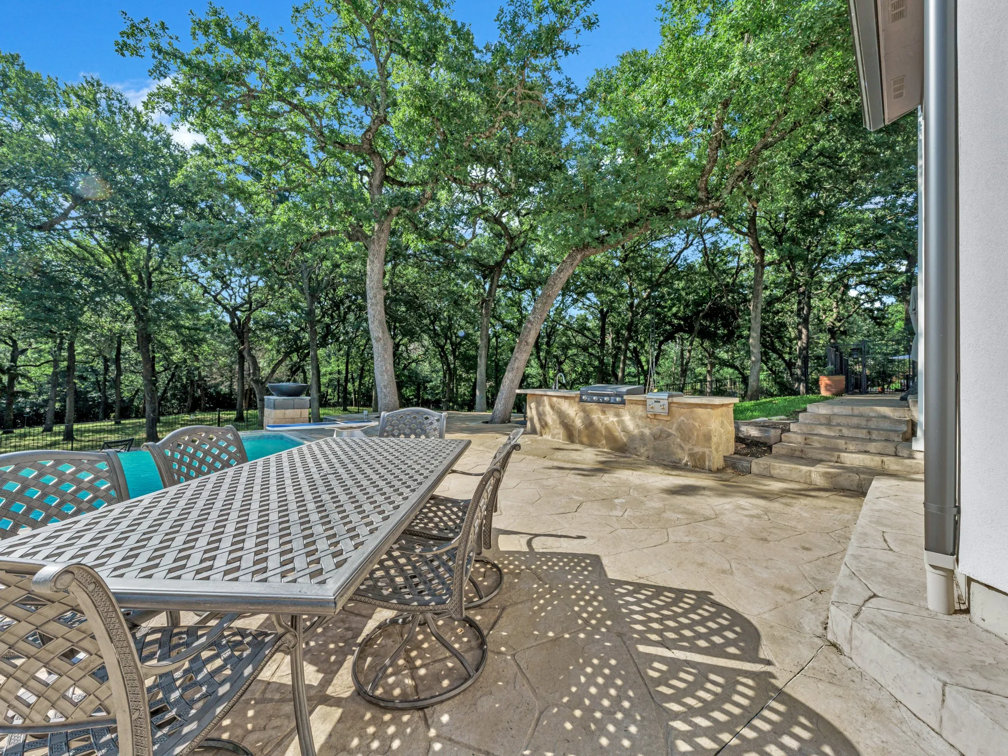 Expansive outdoor patio featuring an integrated outdoor kitchen, stone steps, and a stamped concrete surface