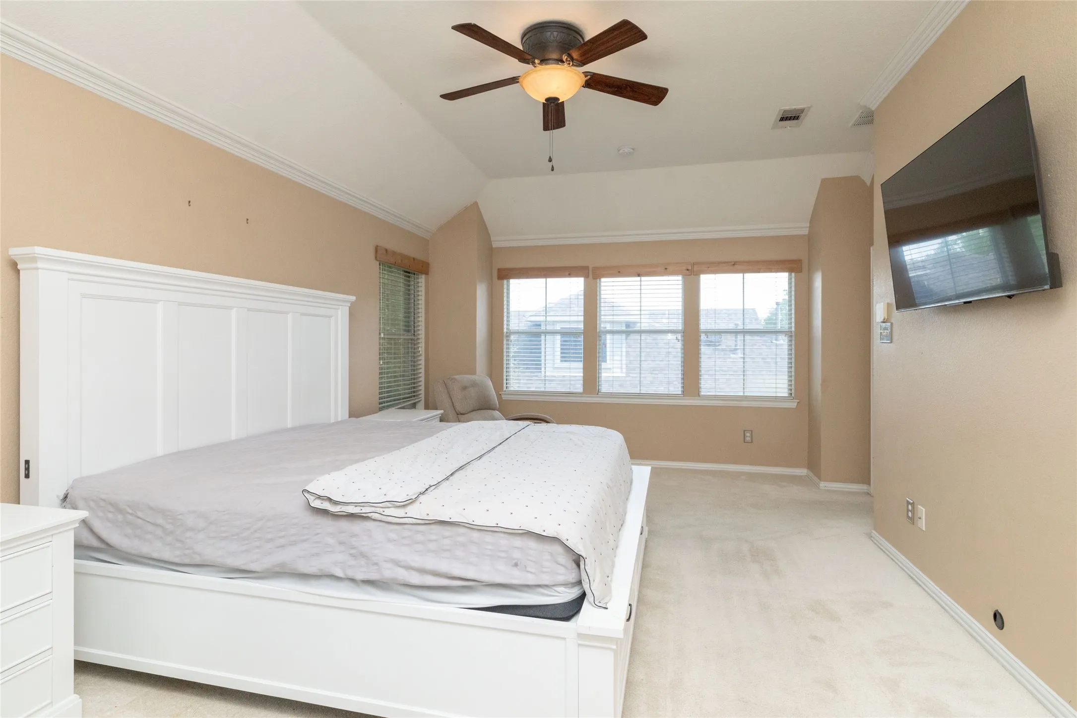 Vaulted ceiling room featuring a ceiling fan with light fixture, triple windows with horizontal blinds, neutral-toned carpeting, and crown molding