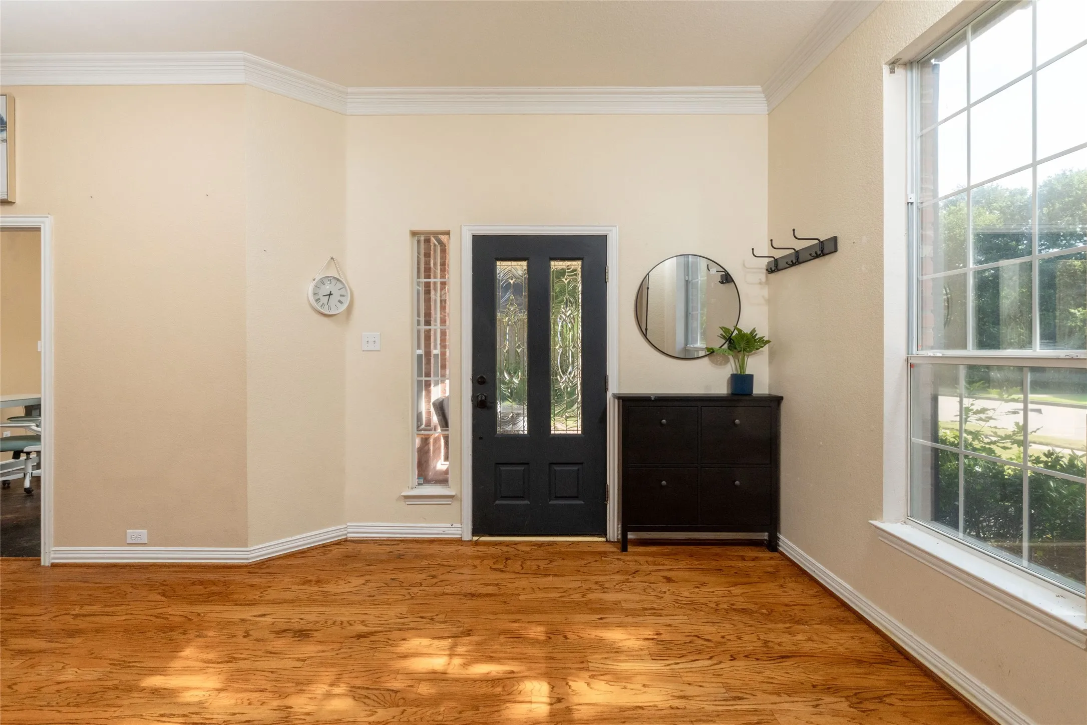 Entryway featuring wood-finish flooring, a dark-paneled front door with decorative glass inserts, and a large window with grid panes