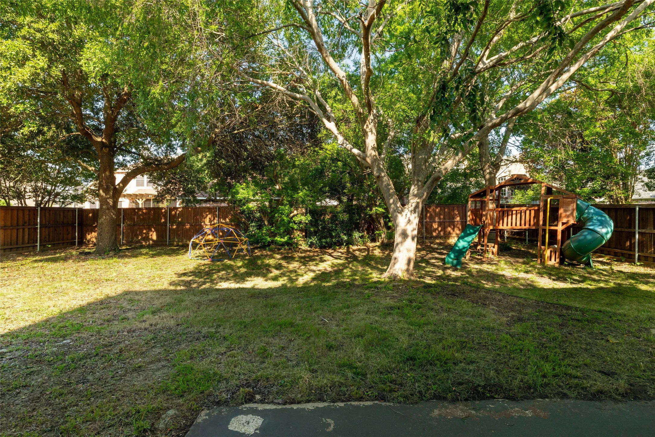 Expansive green space featuring established mature trees, a privacy fence, and a designated play area