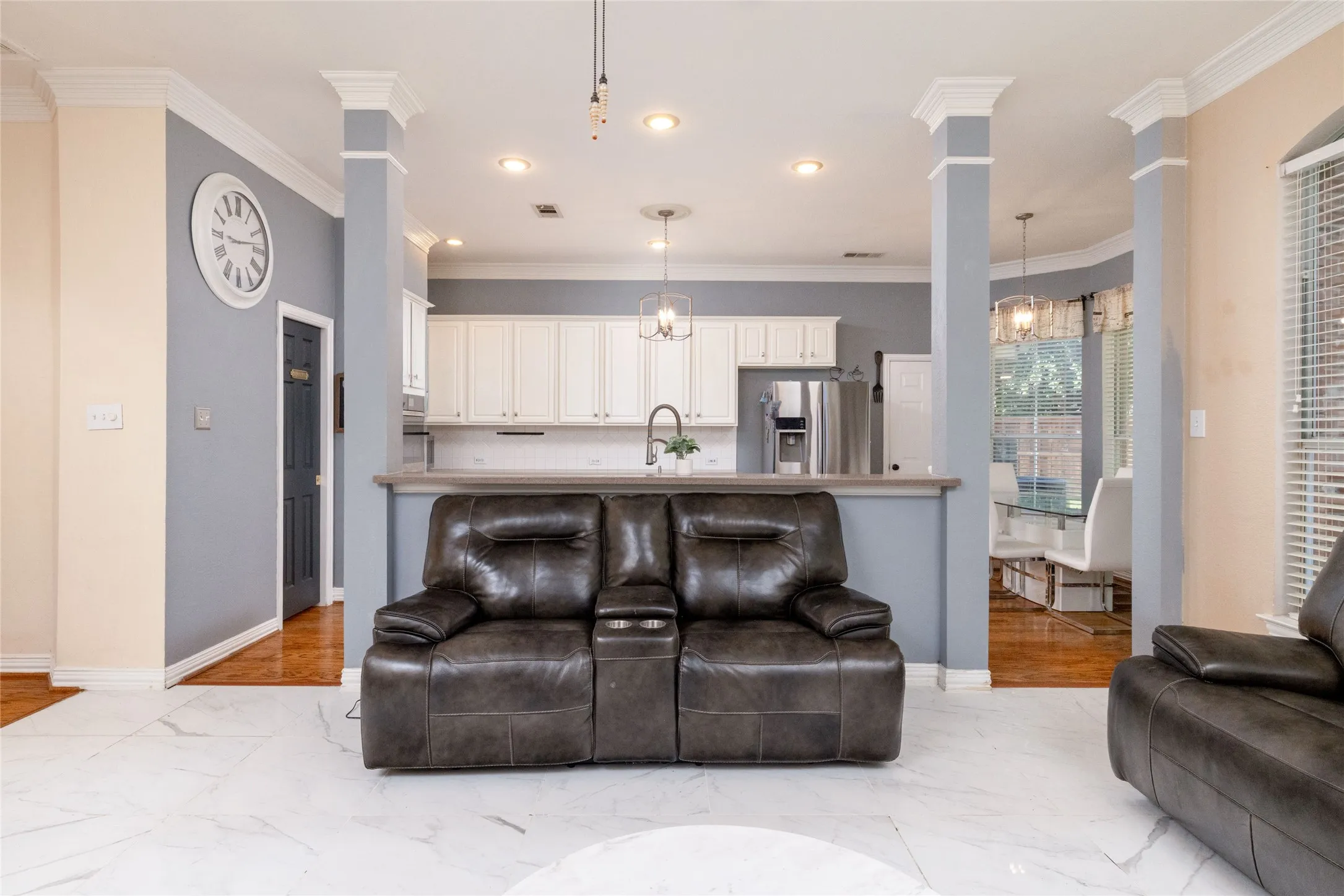 Open-concept living space featuring white marble-finish flooring and crown molding