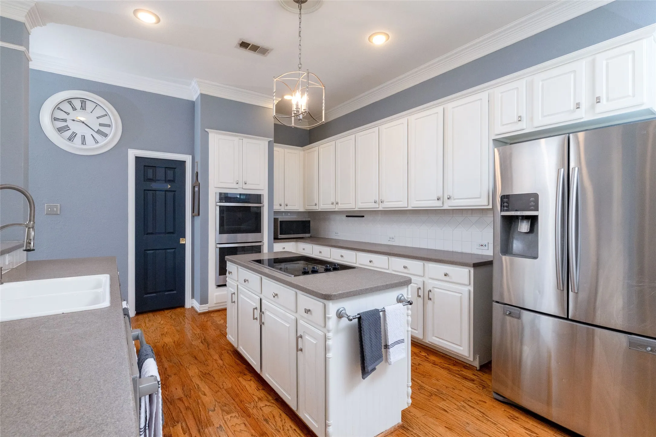 Kitchen featuring a central island with cooktop, white cabinetry, integrated stainless steel appliances, wood-finish flooring, and recessed lighting