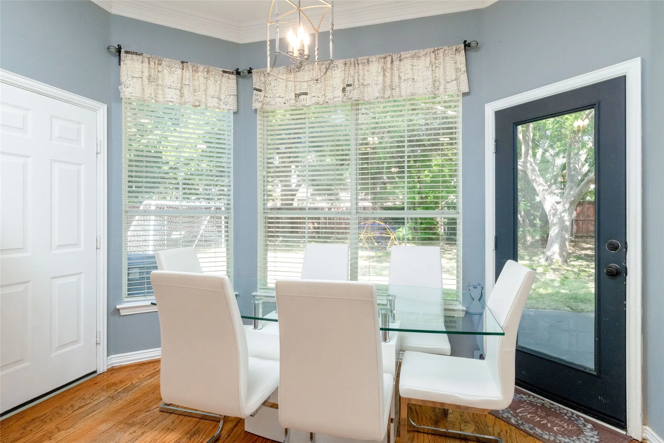 Bay window area featuring wood-finish flooring, light blue wall paint, a white paneled door, and a black-framed glass door providing exterior access