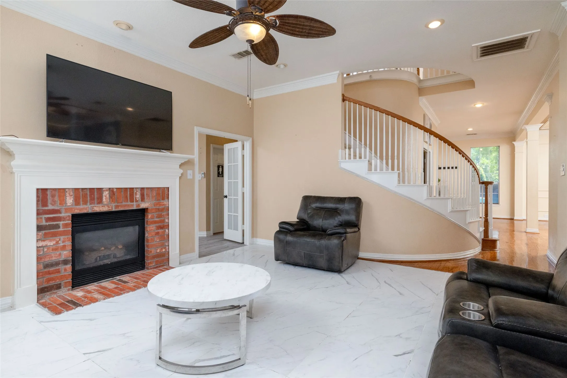 Spacious living area featuring a curved staircase with white balusters and wood-finish handrails, a brick fireplace with a white mantel, and white tile flooring