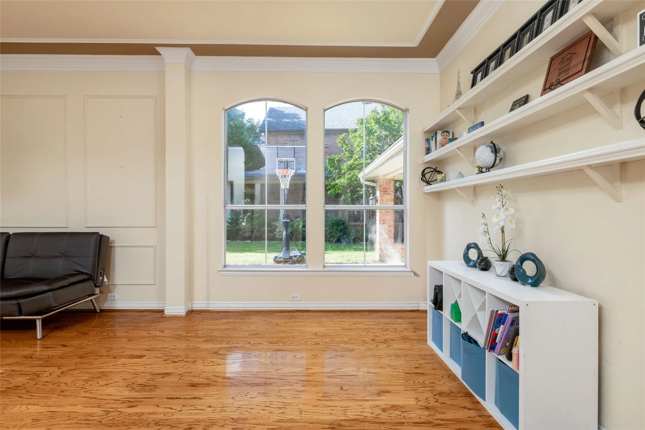 Spacious room featuring wood-finish flooring, two arched windows, crown molding, and wainscoting