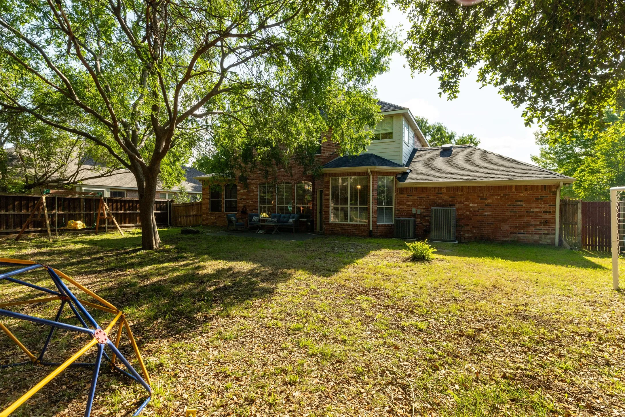 Expansive backyard featuring mature trees, a privacy fence, and a brick exterior with a bay window