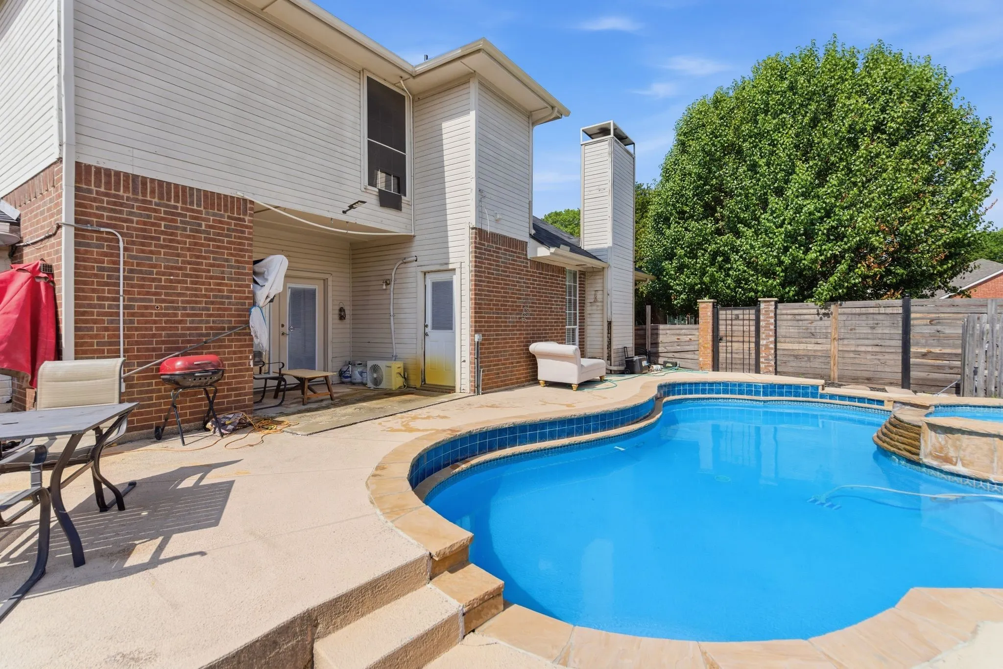Backyard oasis featuring a curvilinear pool with blue tile edging, integrated spa, and a concrete patio