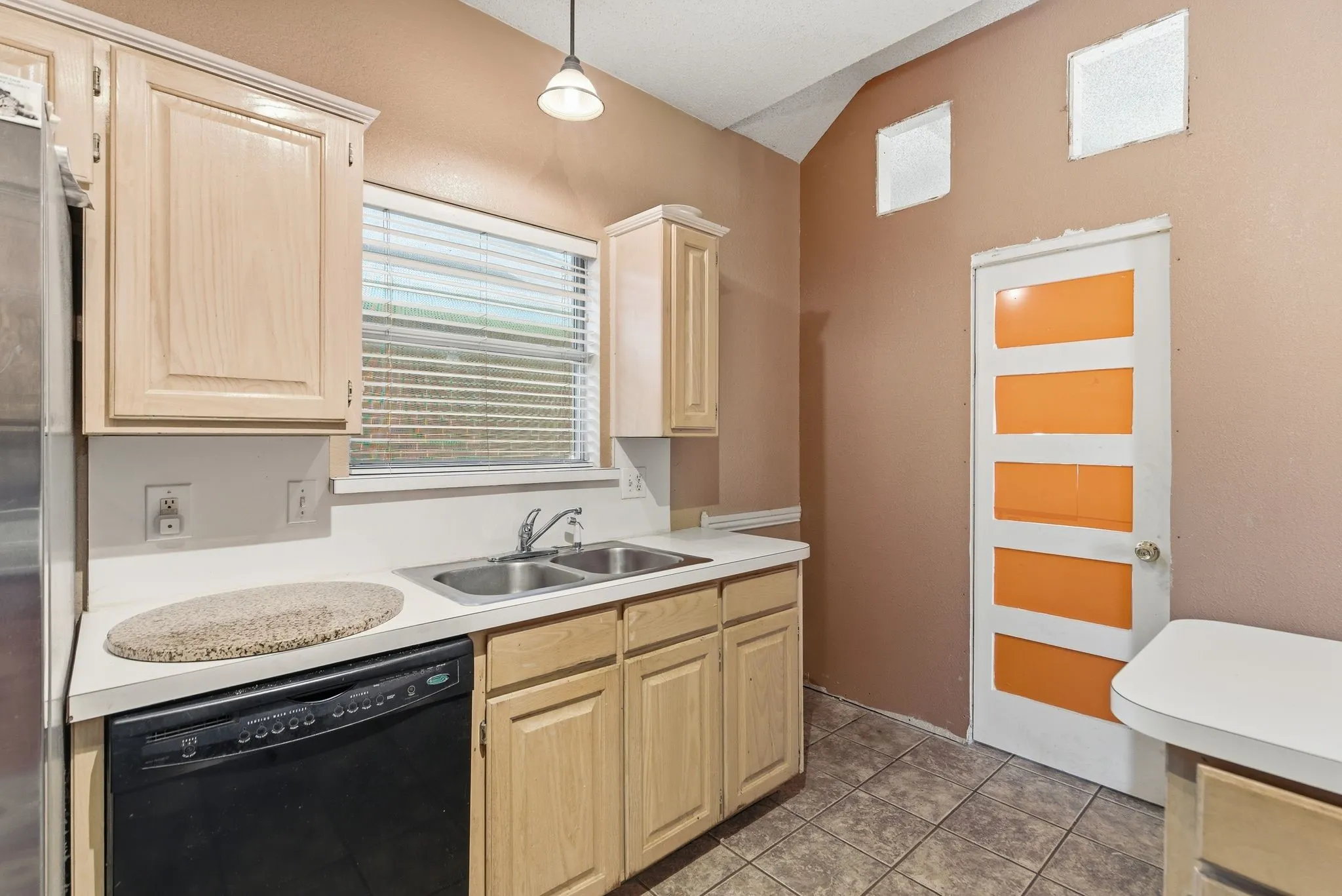 Kitchen space with light wood-finish cabinetry, a double basin stainless steel sink, and a black dishwasher