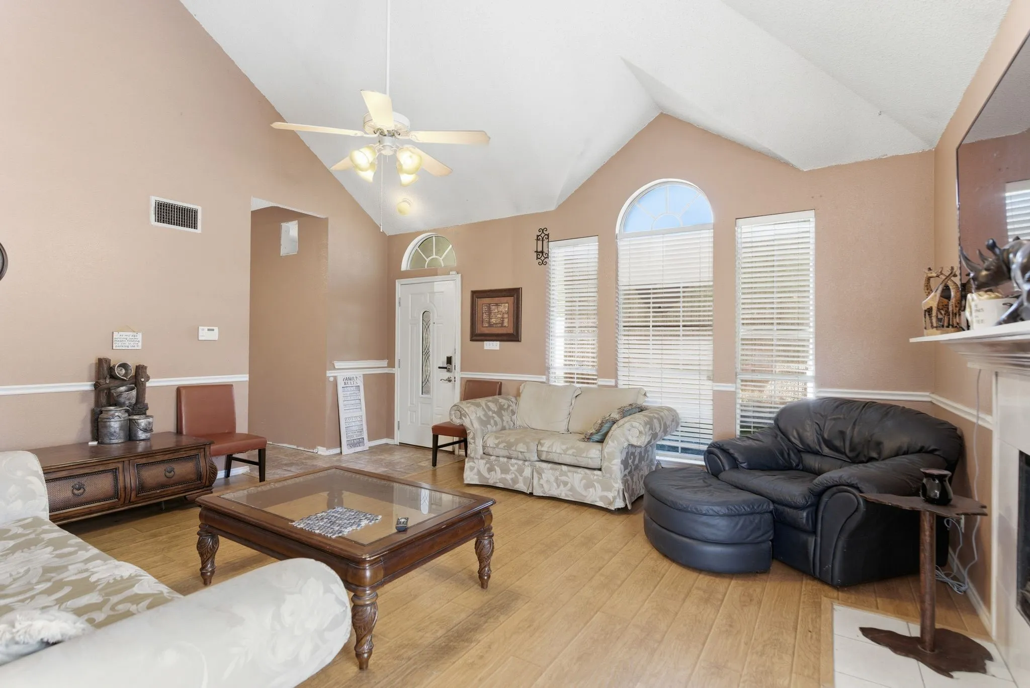 Varying ceiling heights with a vaulted section, wood-finish flooring, white trim details, multiple windows with blinds, and a ceiling fan with integrated lighting