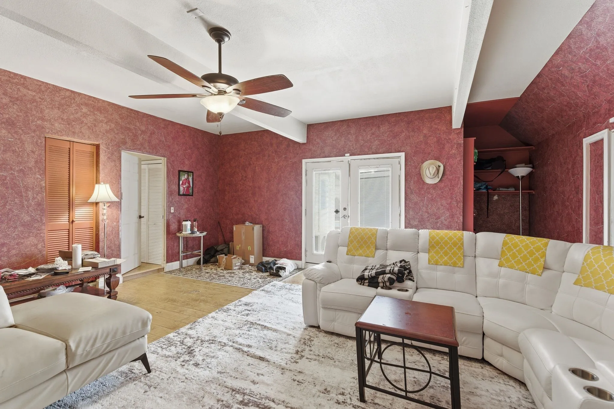 Interior space featuring a ceiling fan with integrated lighting, exposed ceiling beams, and dual glass-paneled doors