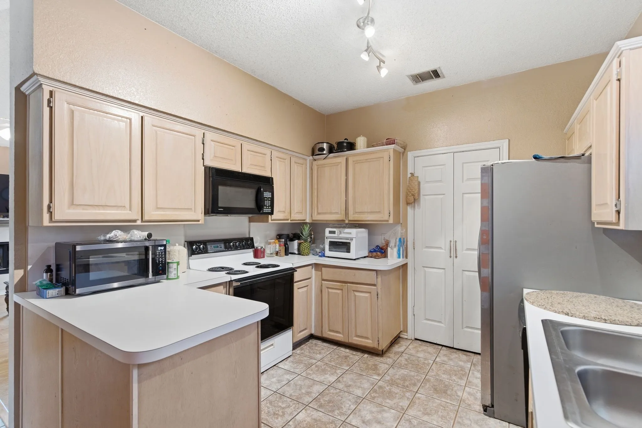 Kitchen featuring light wood-finish cabinetry, white countertops, black built-in microwave, black electric range, and tile flooring