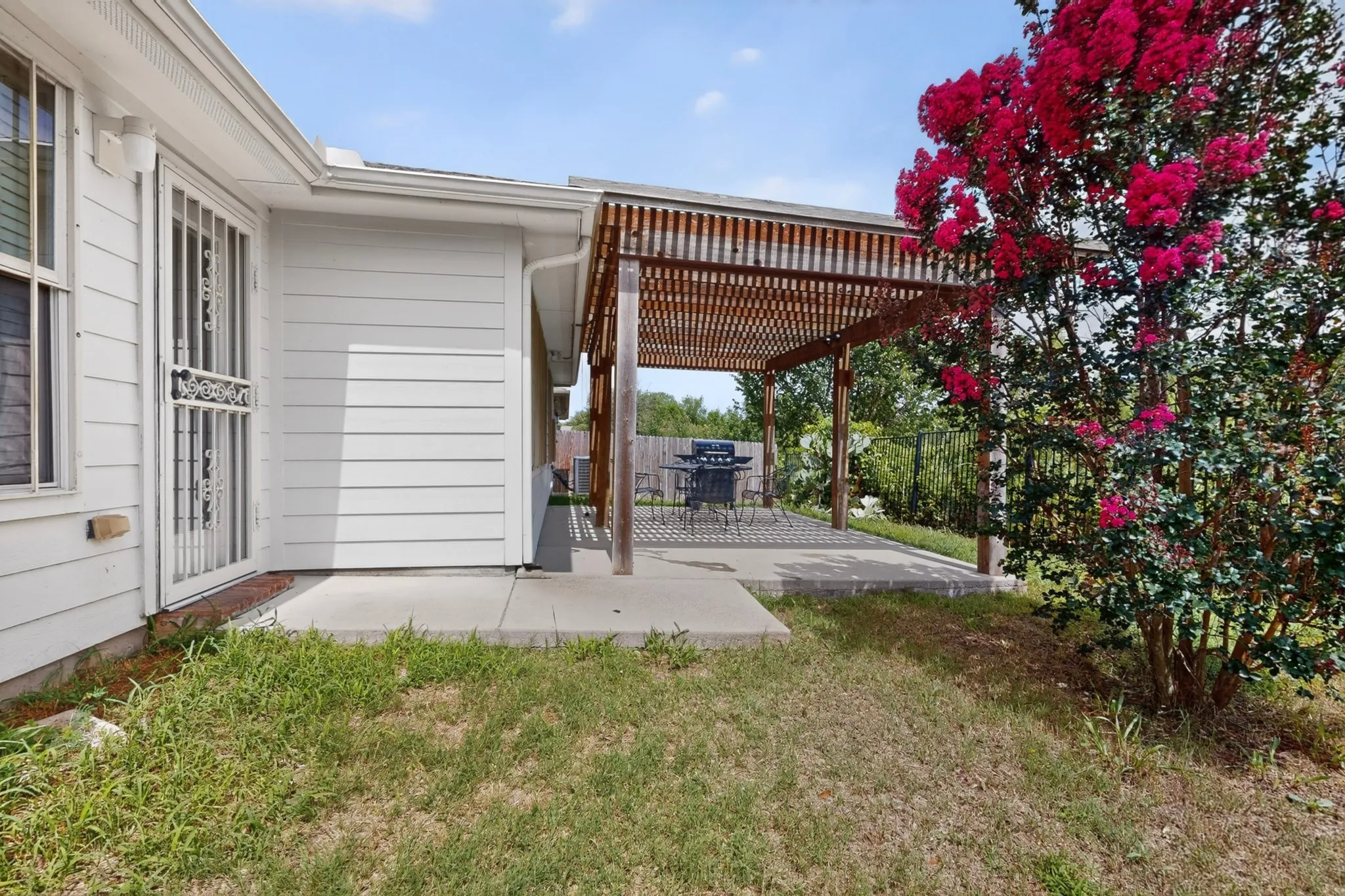 Expansive wooden pergola extending from the home, featuring a concrete patio and lush landscaping
