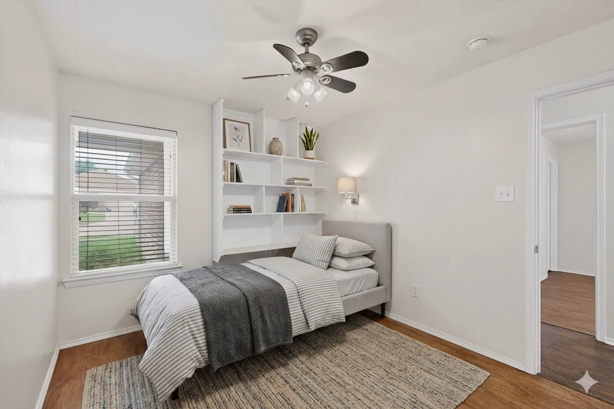 Well-lit room featuring wood-finish flooring, built-in shelving, a ceiling fan with integrated lighting, and a window with blinds