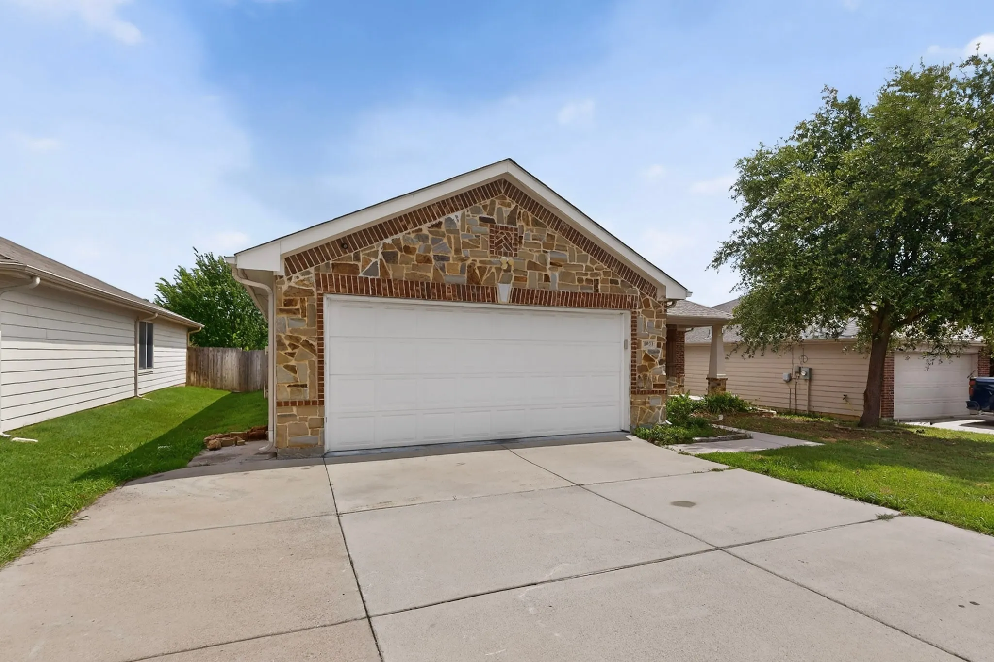 Front exterior featuring a two-car garage with a white door, concrete driveway, and a stone and brick facade
